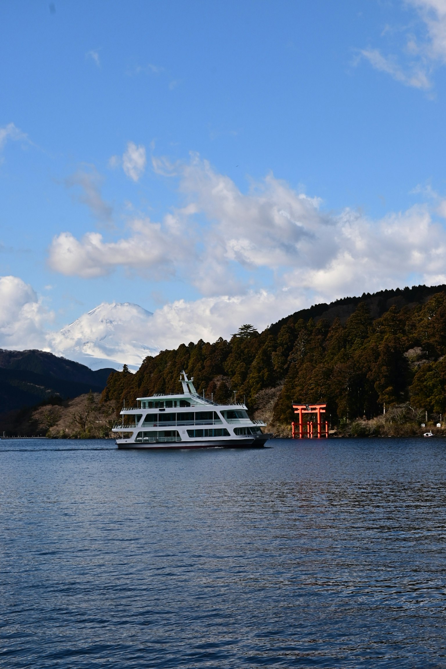 ทิวทัศน์ของทะเลสาบที่สวยงามพร้อมเรือท่องเที่ยวและประตูโทริอิสีแดงใต้ท้องฟ้าสีฟ้า