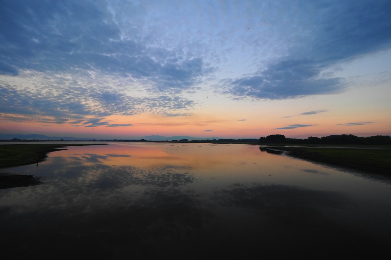 Acqua tranquilla che riflette un cielo al tramonto colorato e nuvole