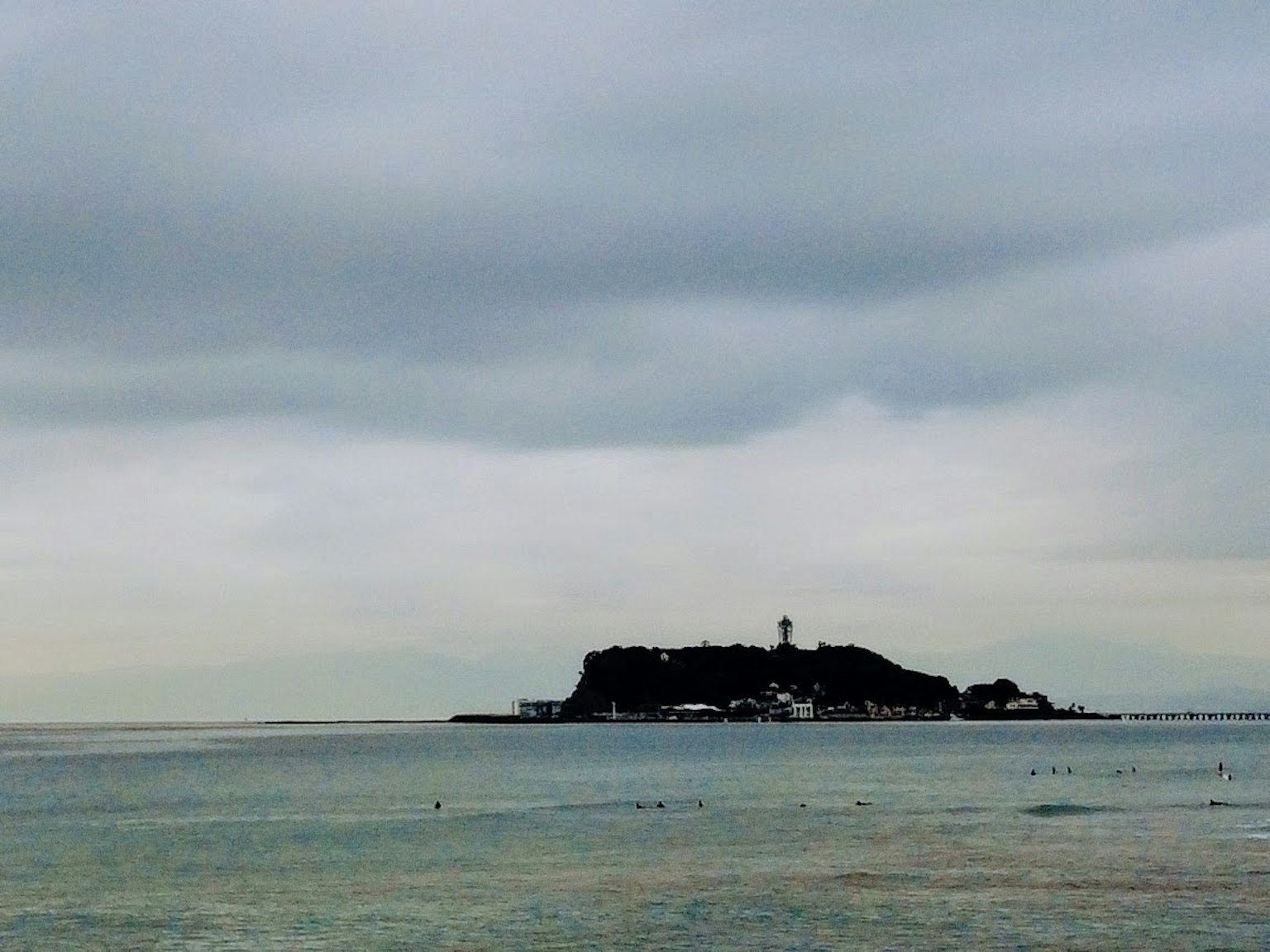 A small island with a lighthouse under a cloudy sky