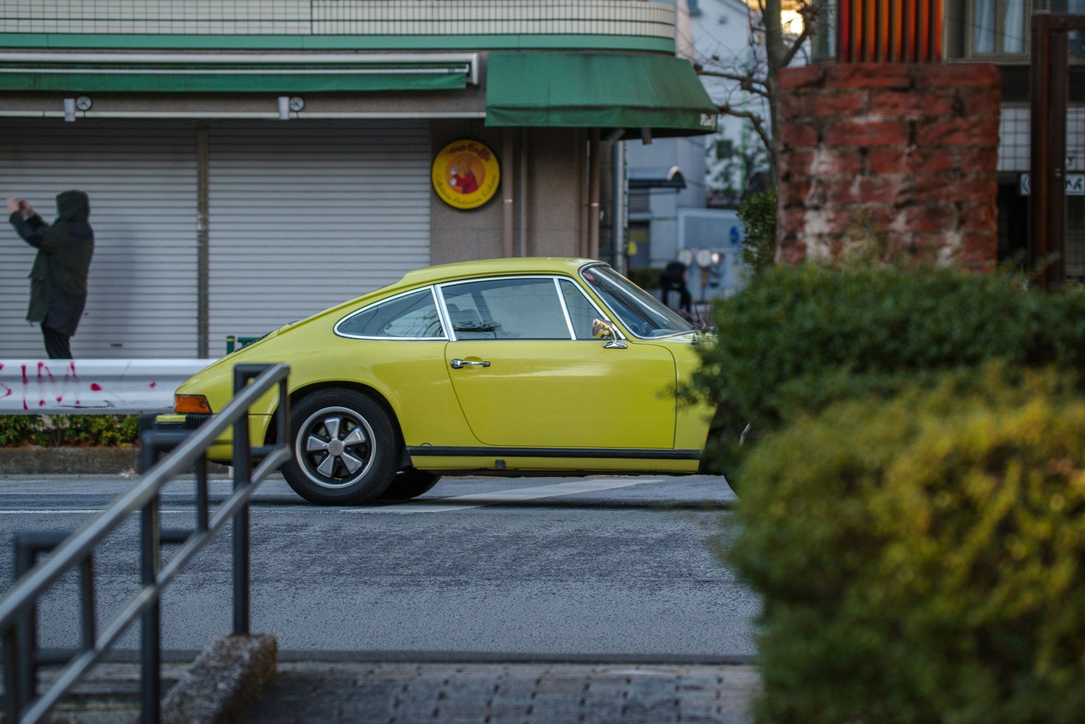 Sebuah Porsche kuning diparkir di jalan dengan penutup toko dan seseorang di latar belakang