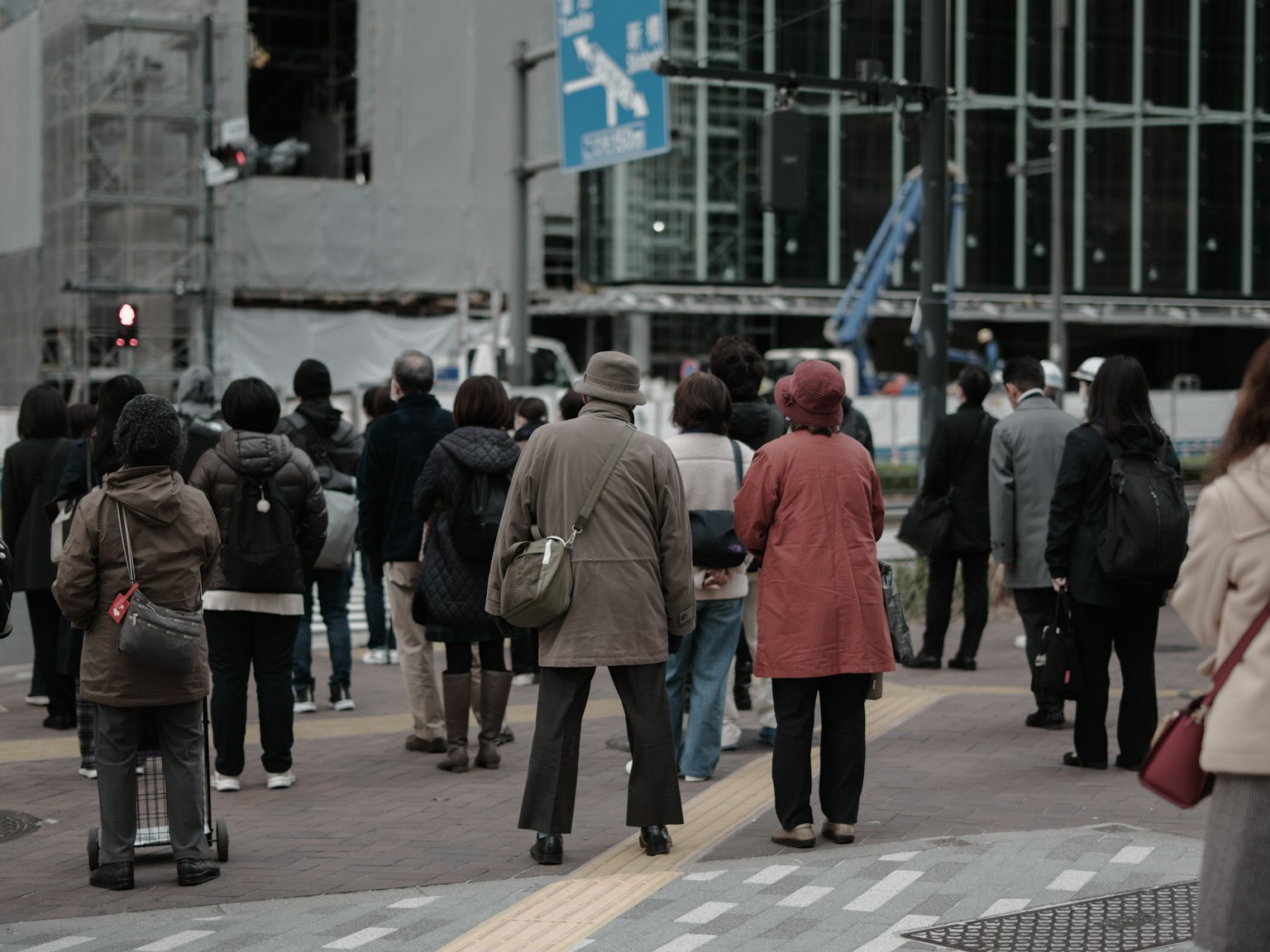 Sekelompok orang menunggu di zebra cross seorang wanita dengan mantel merah menonjol