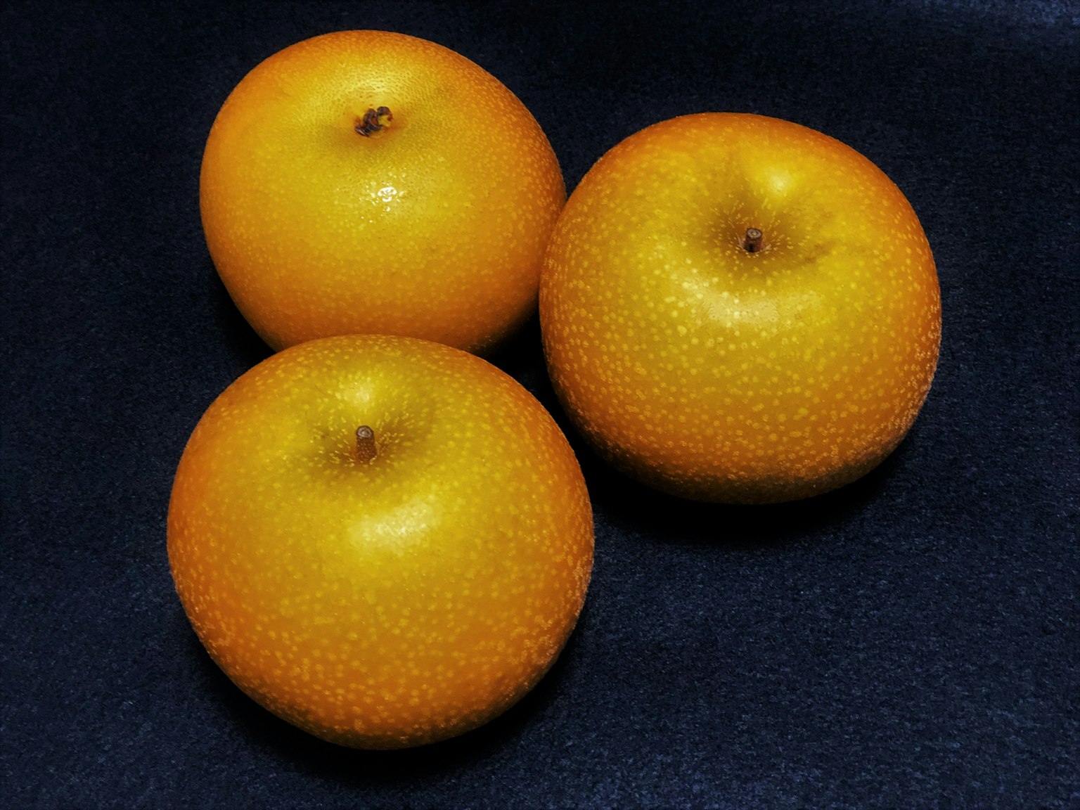 Trois fruits orange disposés sur un fond noir