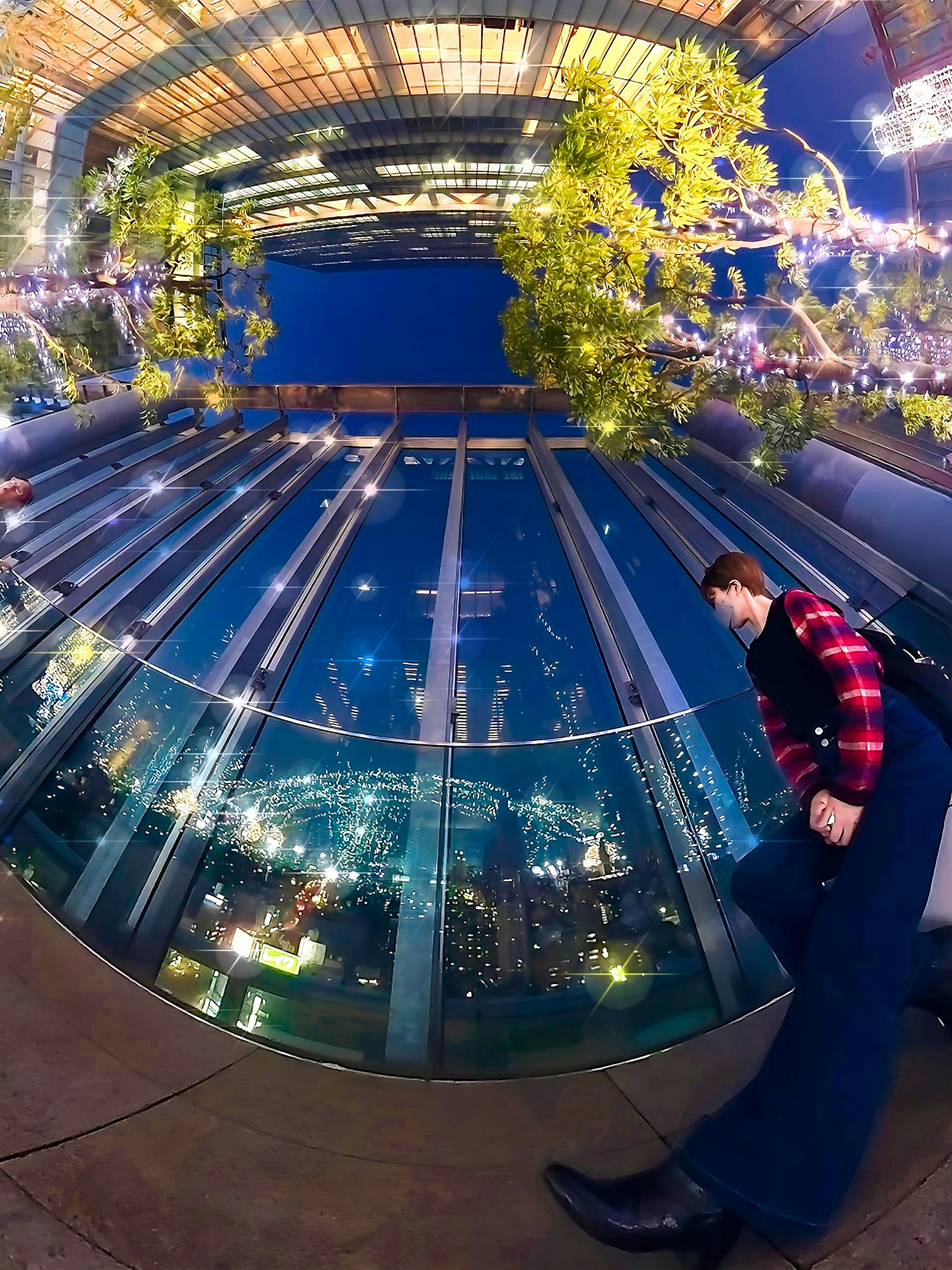 Une personne marchant sur un balcon en verre avec des lumières de la ville en arrière-plan