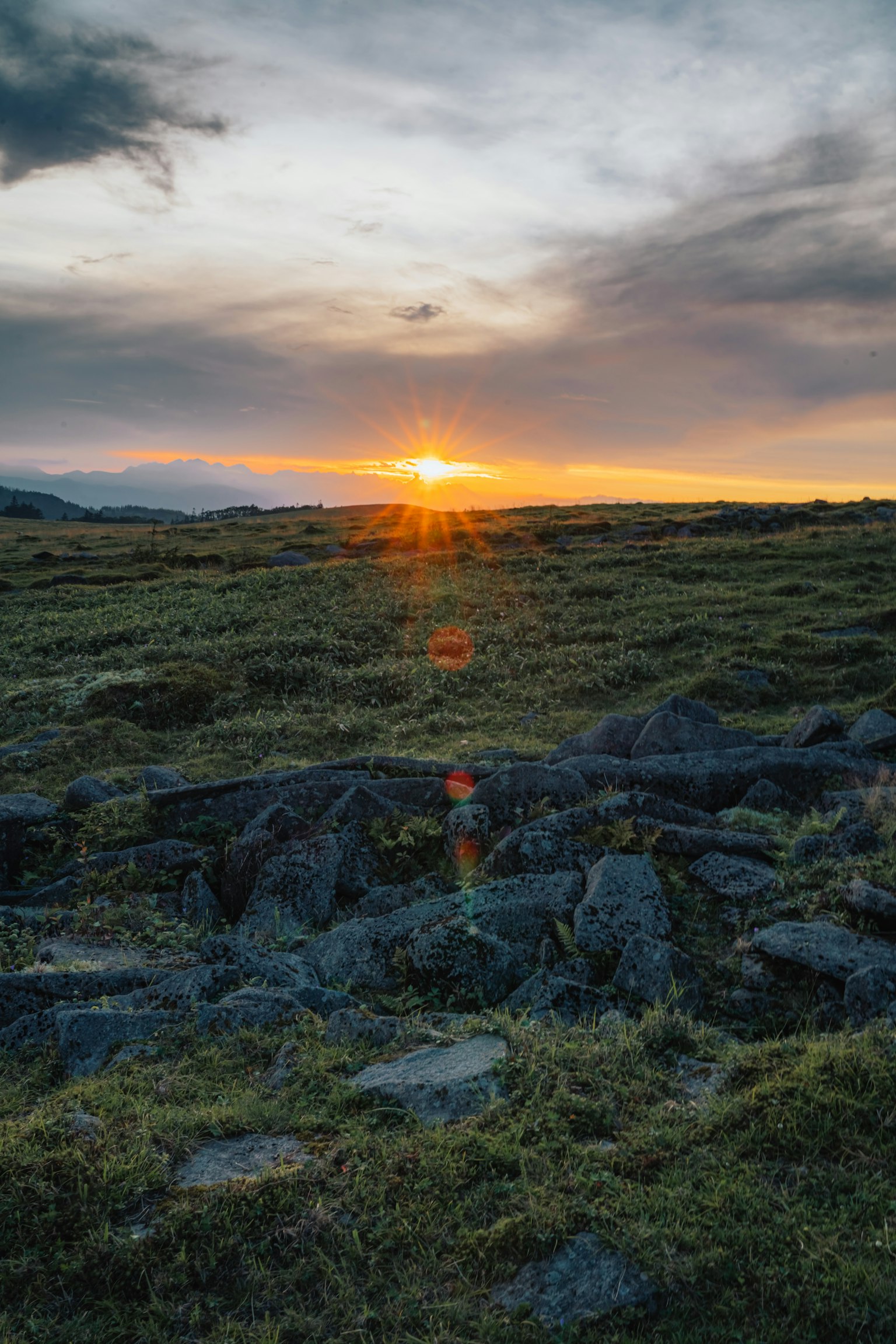 Atardecer sobre un paisaje rocoso con hierba verde y cielo nublado