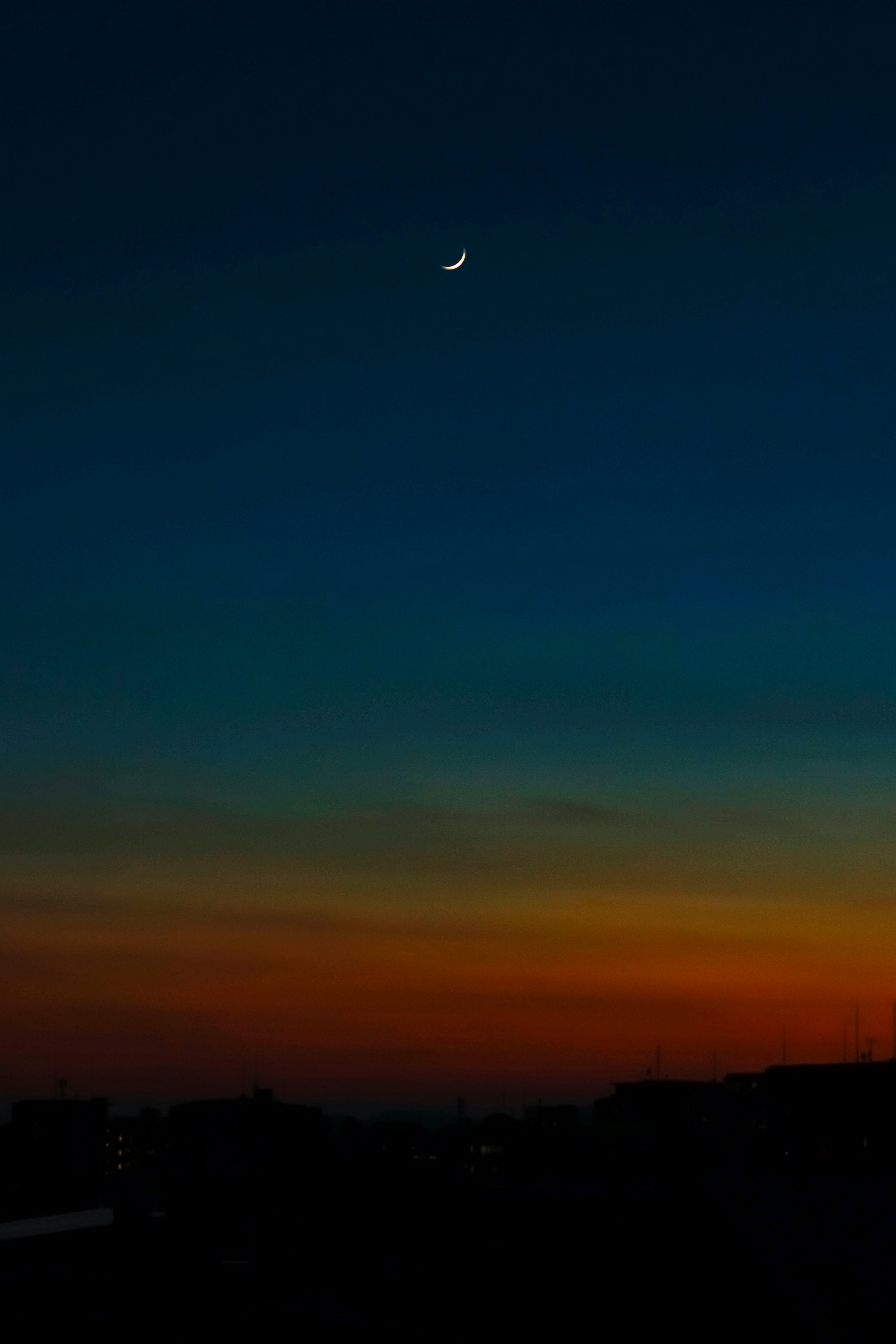 薄明の空に浮かぶ月と夕焼けの夜空