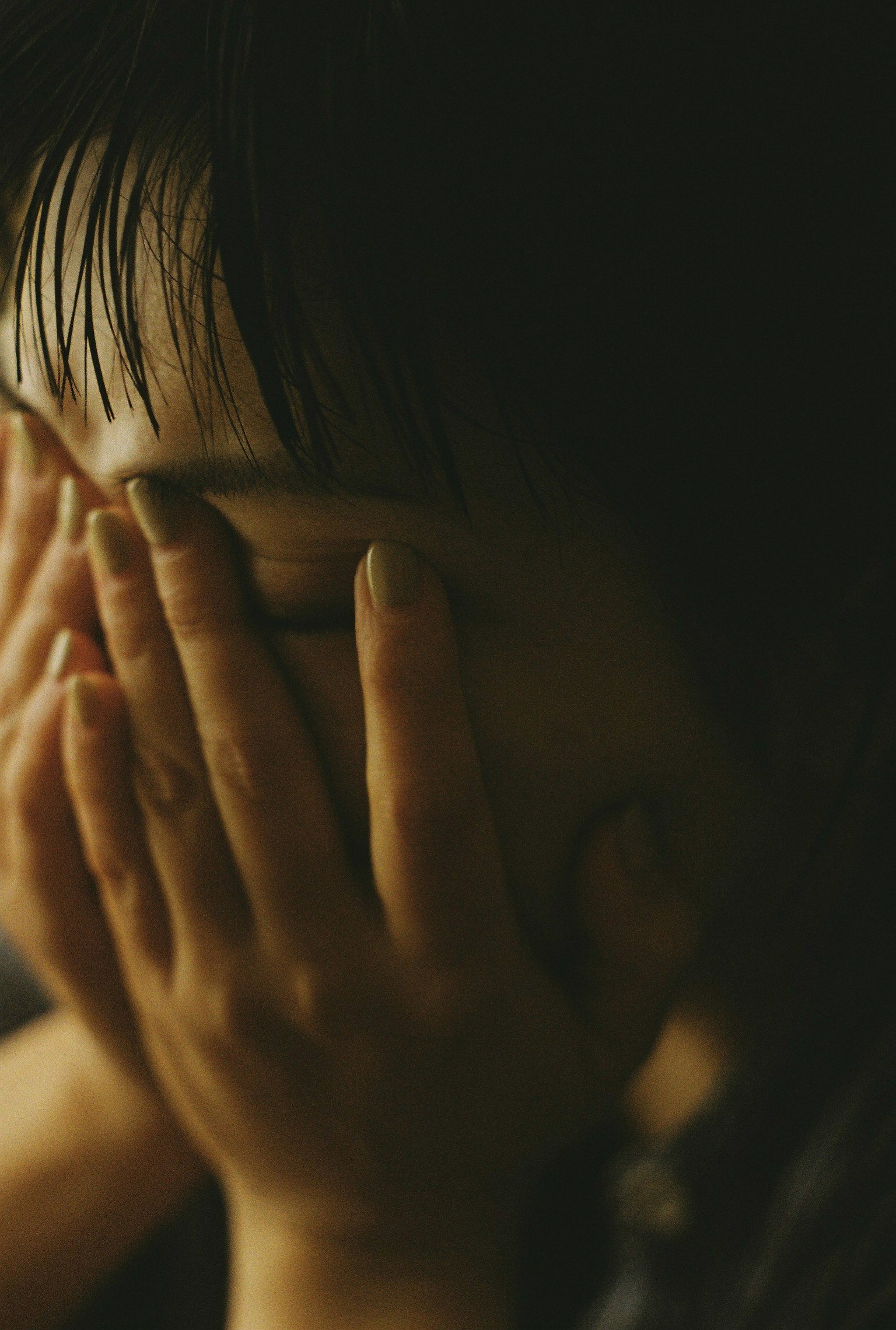 子供が手で顔を覆っている様子 暗い背景で感情を表現