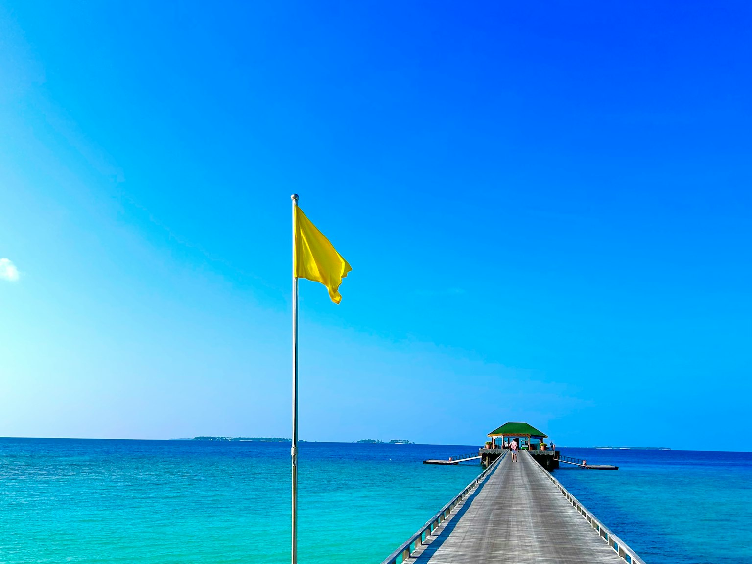 Holzsteg mit einer gelben Flagge vor blauem Himmel und Meer