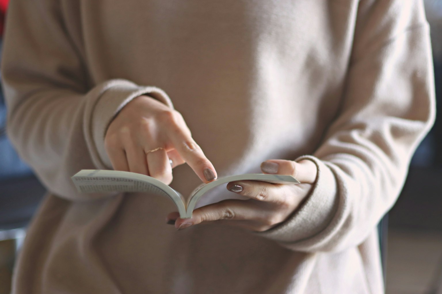 Woman in a light sweater pointing at a book