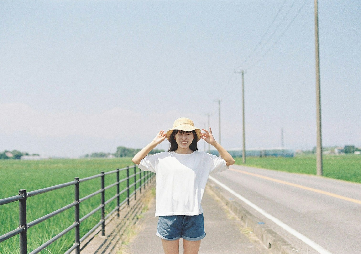 田園の道沿いで帽子をかぶる女性