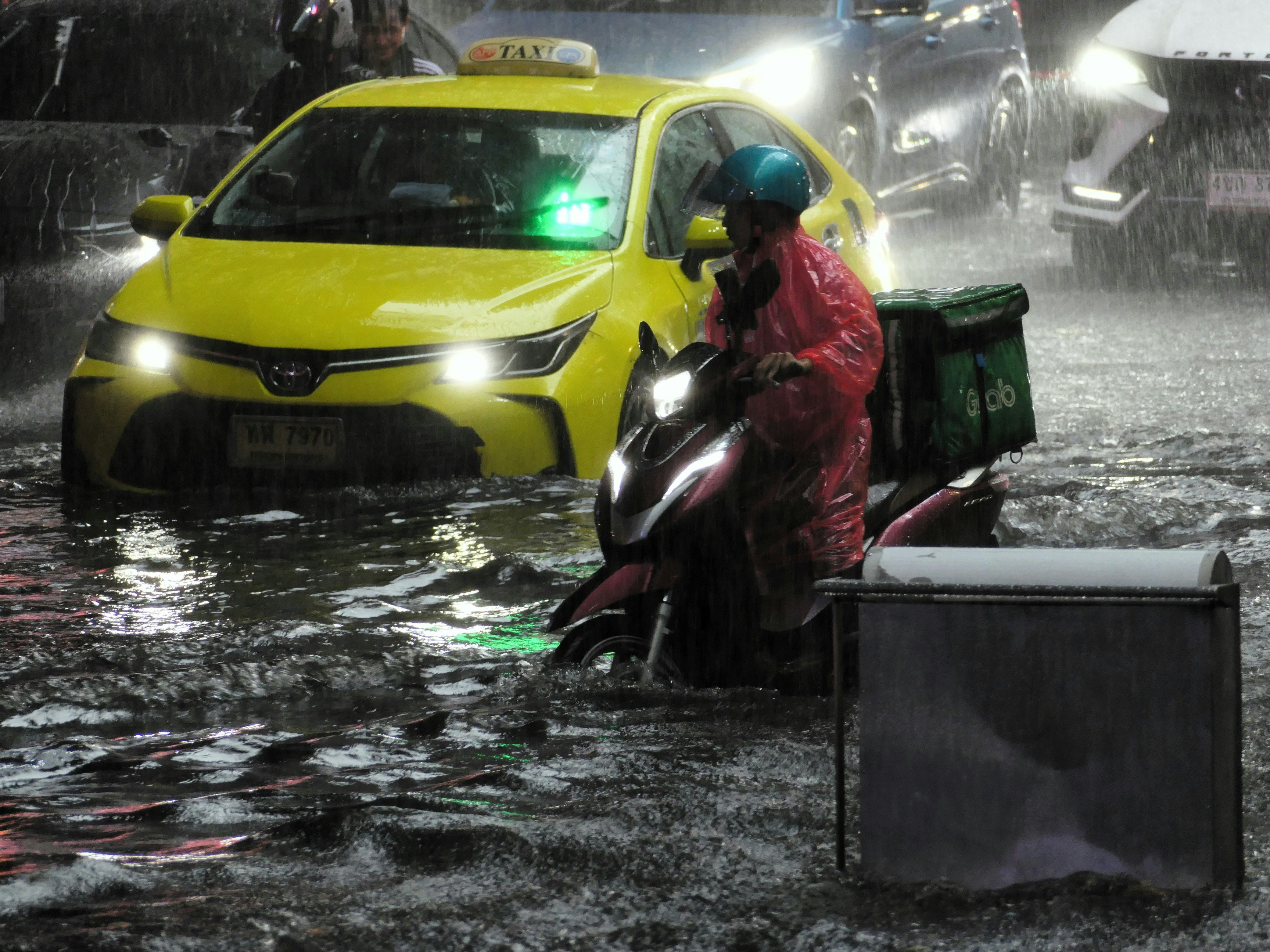 雨の夜にタクシーの前を走るバイクと歩行者
