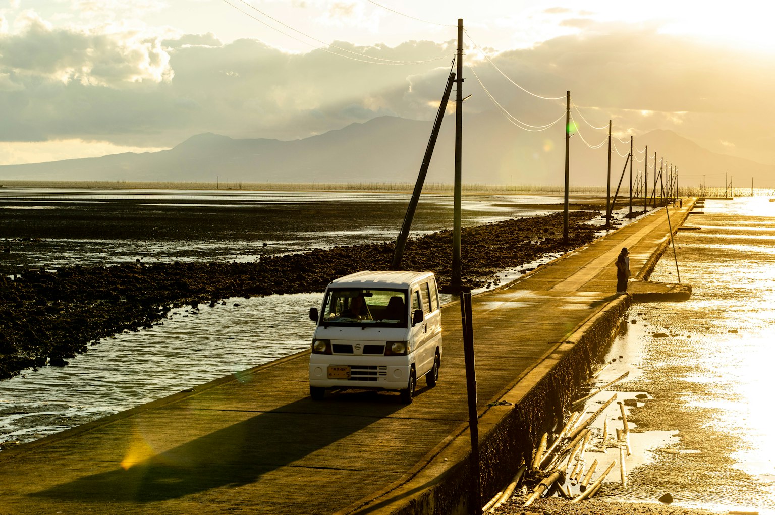 Un fourgon blanc circulant sur une route côtière entourée d'eau et de coucher de soleil