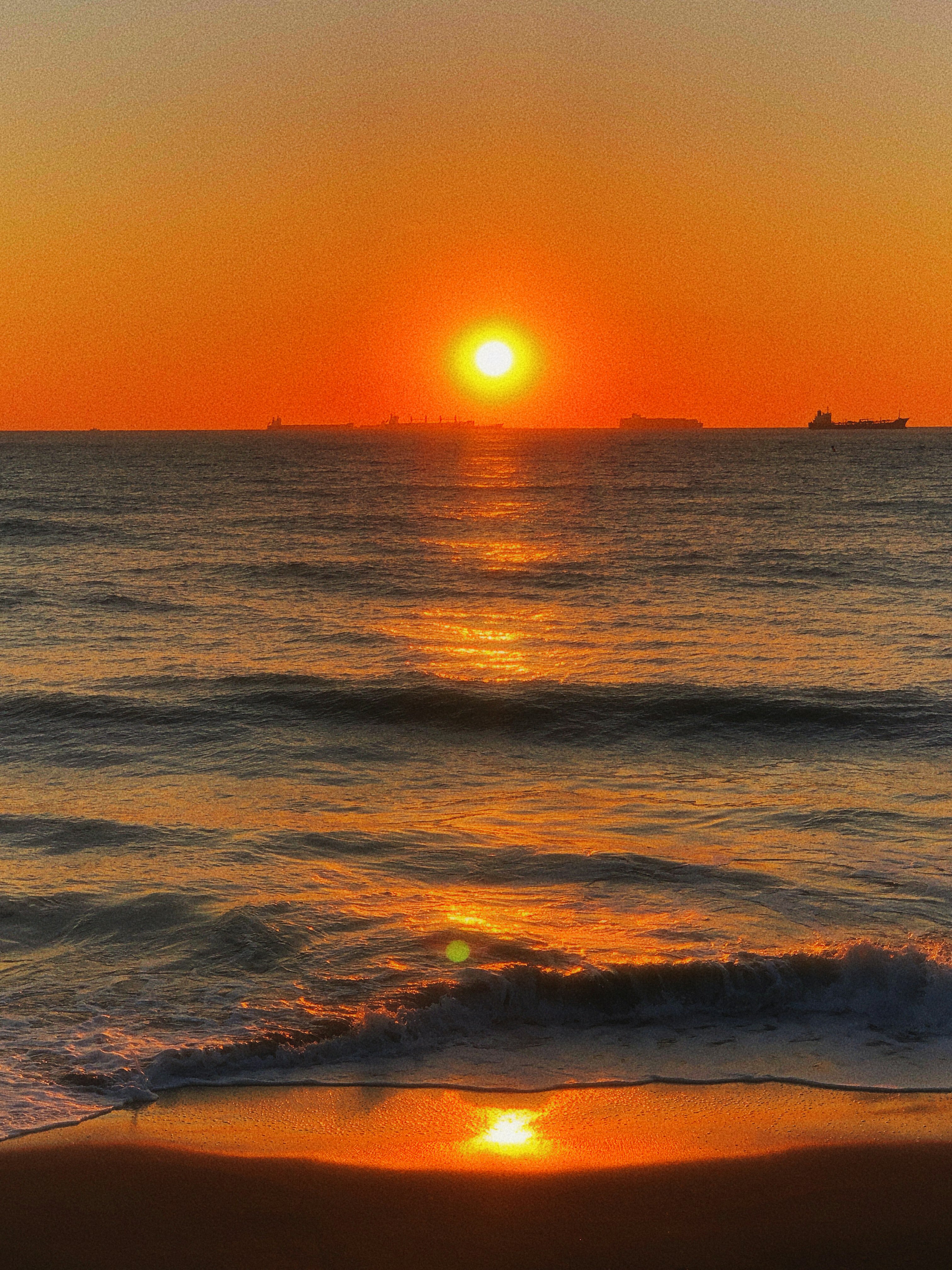 sunset over the horizon with ocean waves at the shoreline