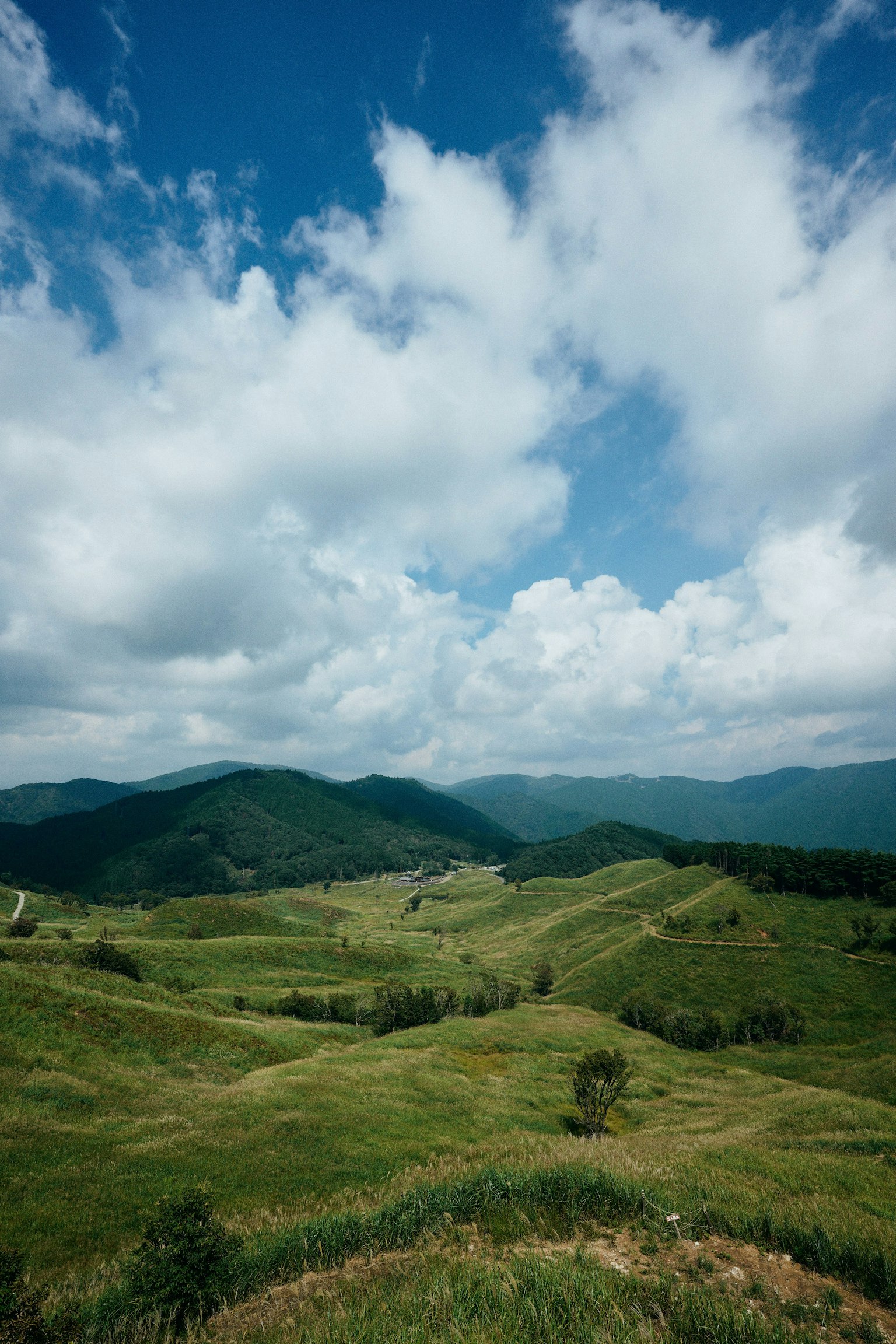 ภูมิทัศน์ของเนินเขาสีเขียวภายใต้ท้องฟ้าสีฟ้าพร้อมเมฆสีขาว
