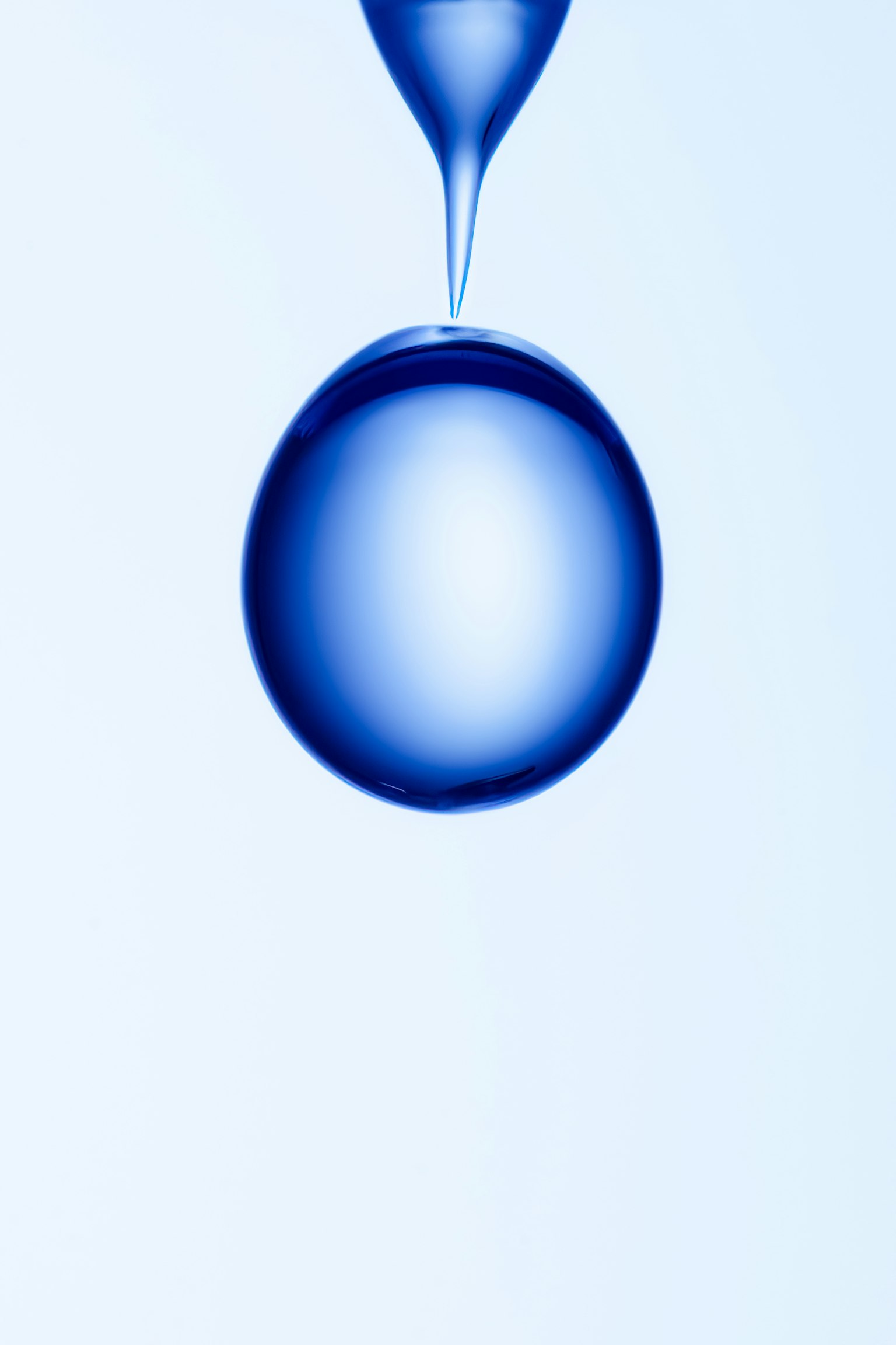 A blue water droplet suspended from a white background creating a simple and beautiful image