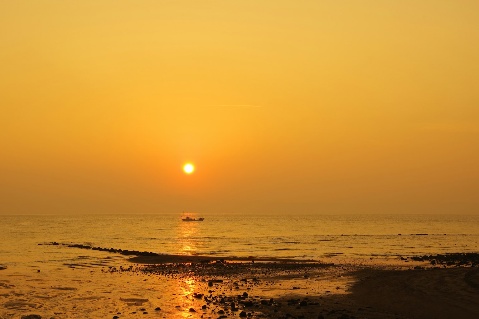 Sunset over the ocean with a golden sky and a distant boat