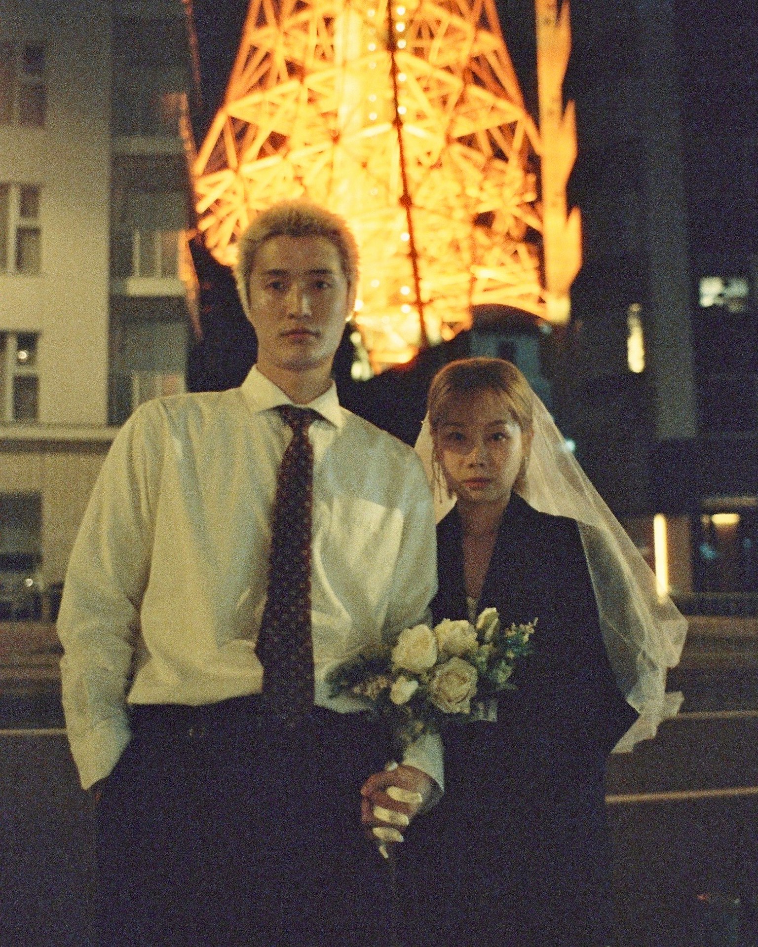 東京タワーの前で結婚式の衣装を着たカップルが立っている夜の写真