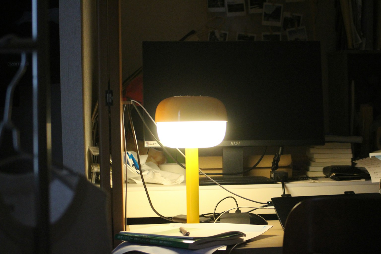 A yellow desk lamp illuminating a workspace with a computer monitor in the background