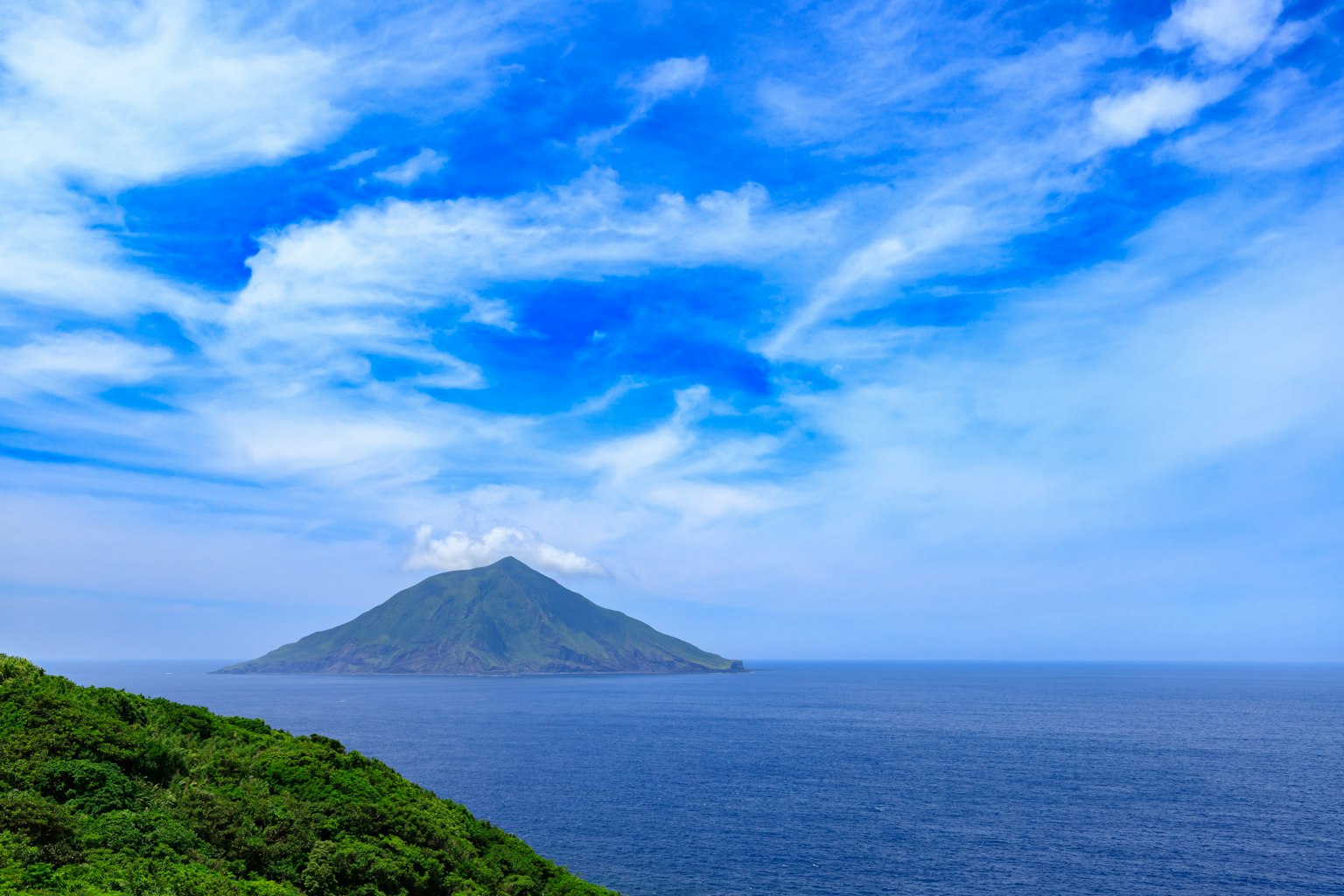 Scenic view of a green island surrounded by blue sky and ocean