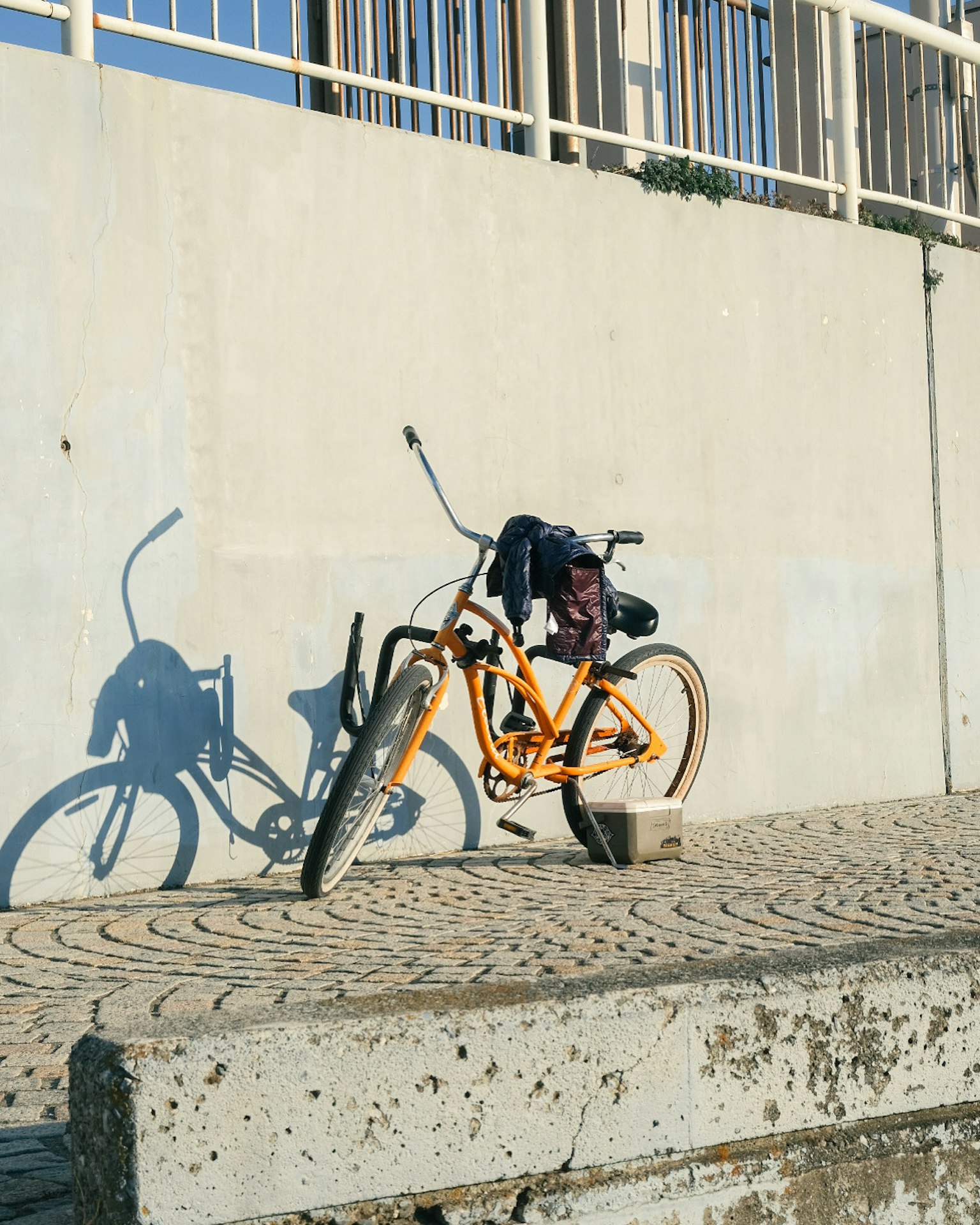 An orange bicycle leaning against a wall casting a shadow