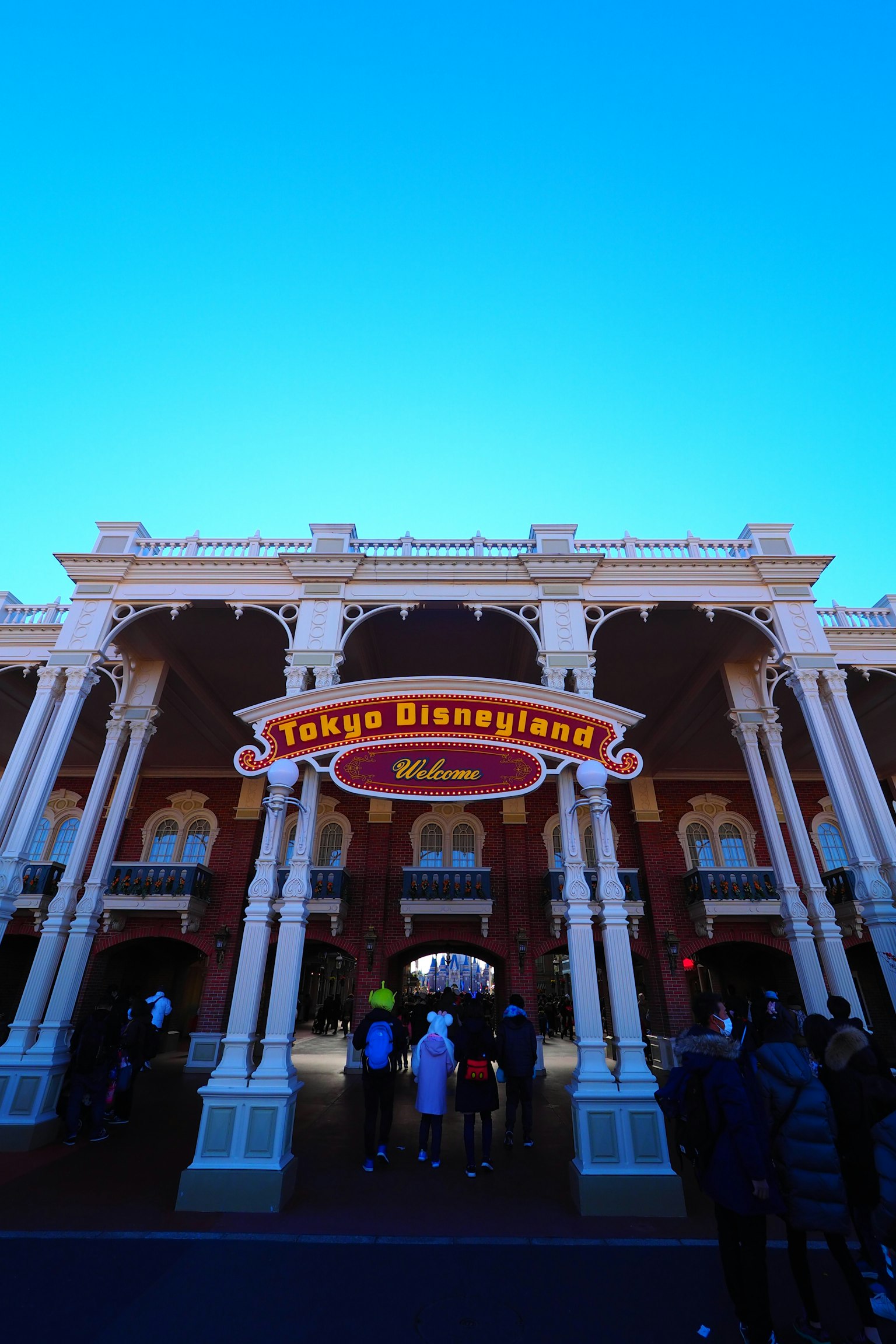 Pintu masuk Tokyo Disneyland dengan tanda berwarna dan langit biru