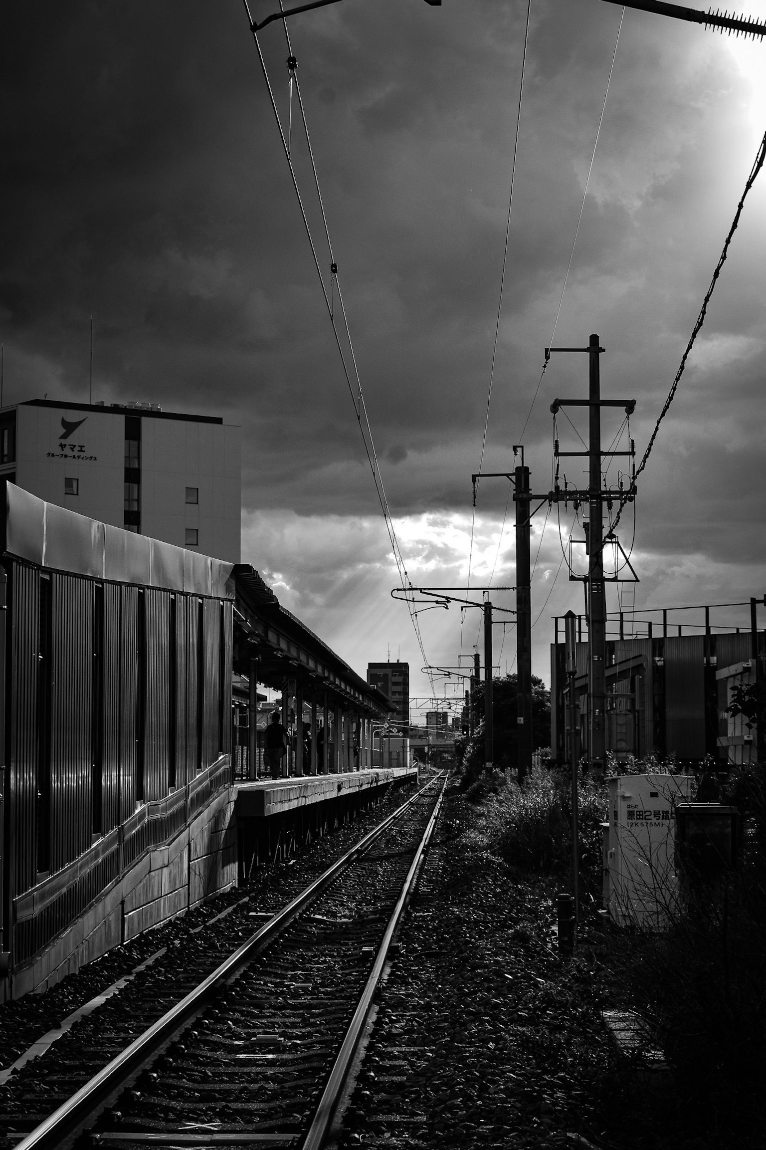 Escena de estación de tren bajo nubes oscuras con vías y postes eléctricos