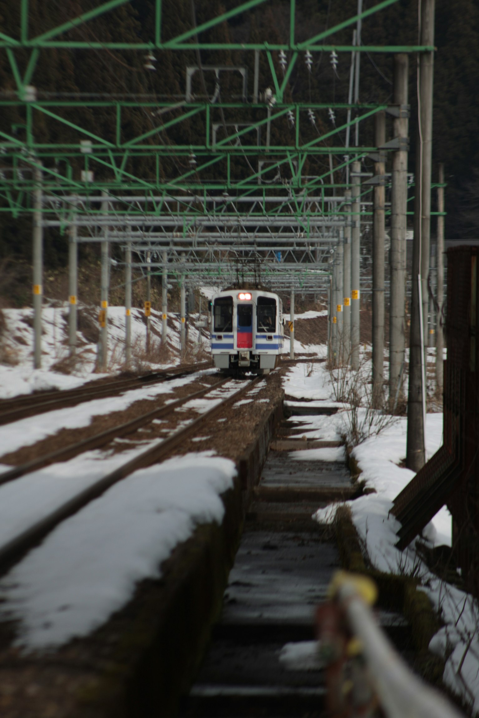 Zug, der auf schneebedeckten Gleisen mit grünen Oberleitungen fährt