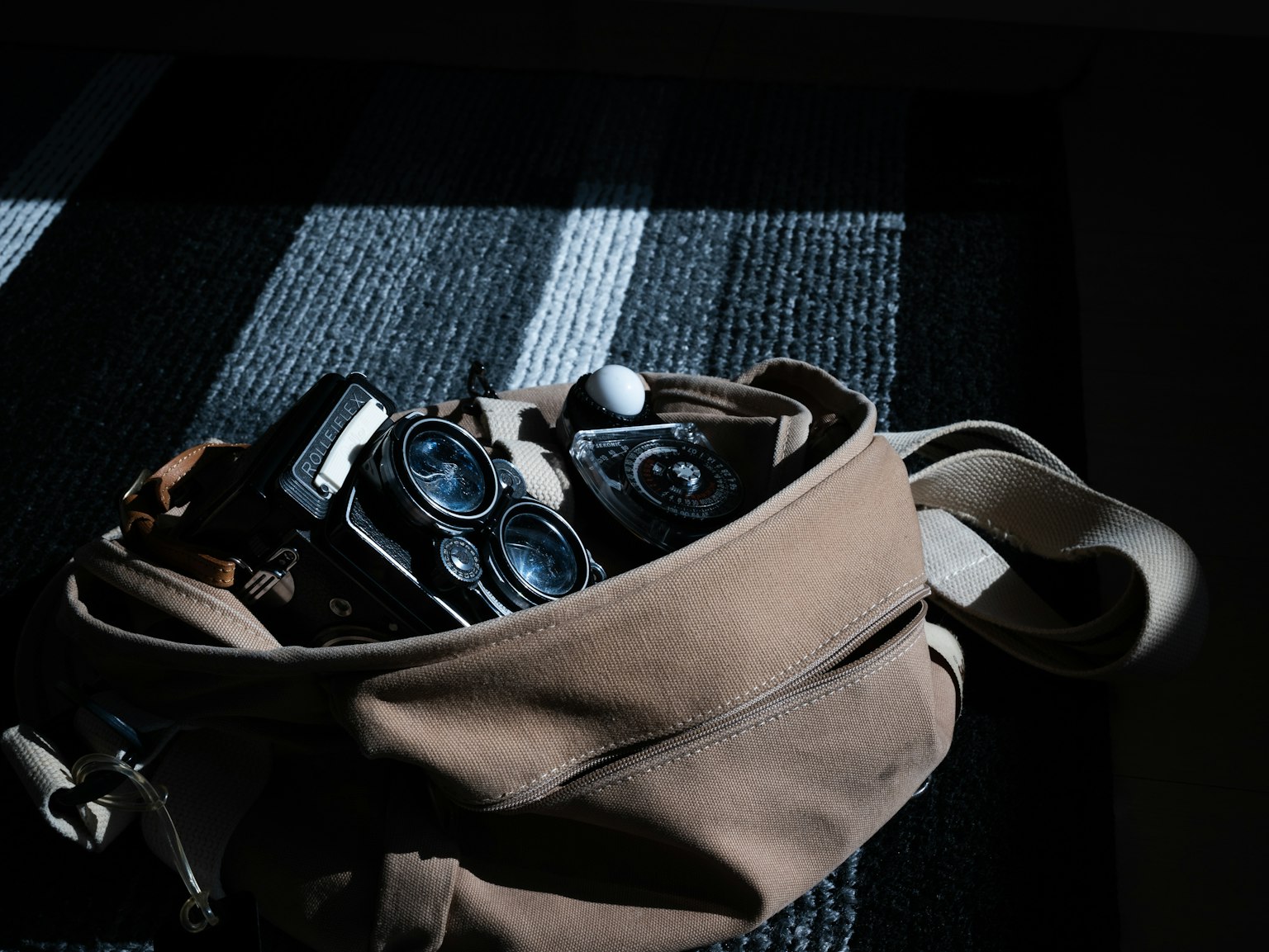 Una borsa marrone piena di fotocamere e vari oggetti poggiata su una superficie a strisce