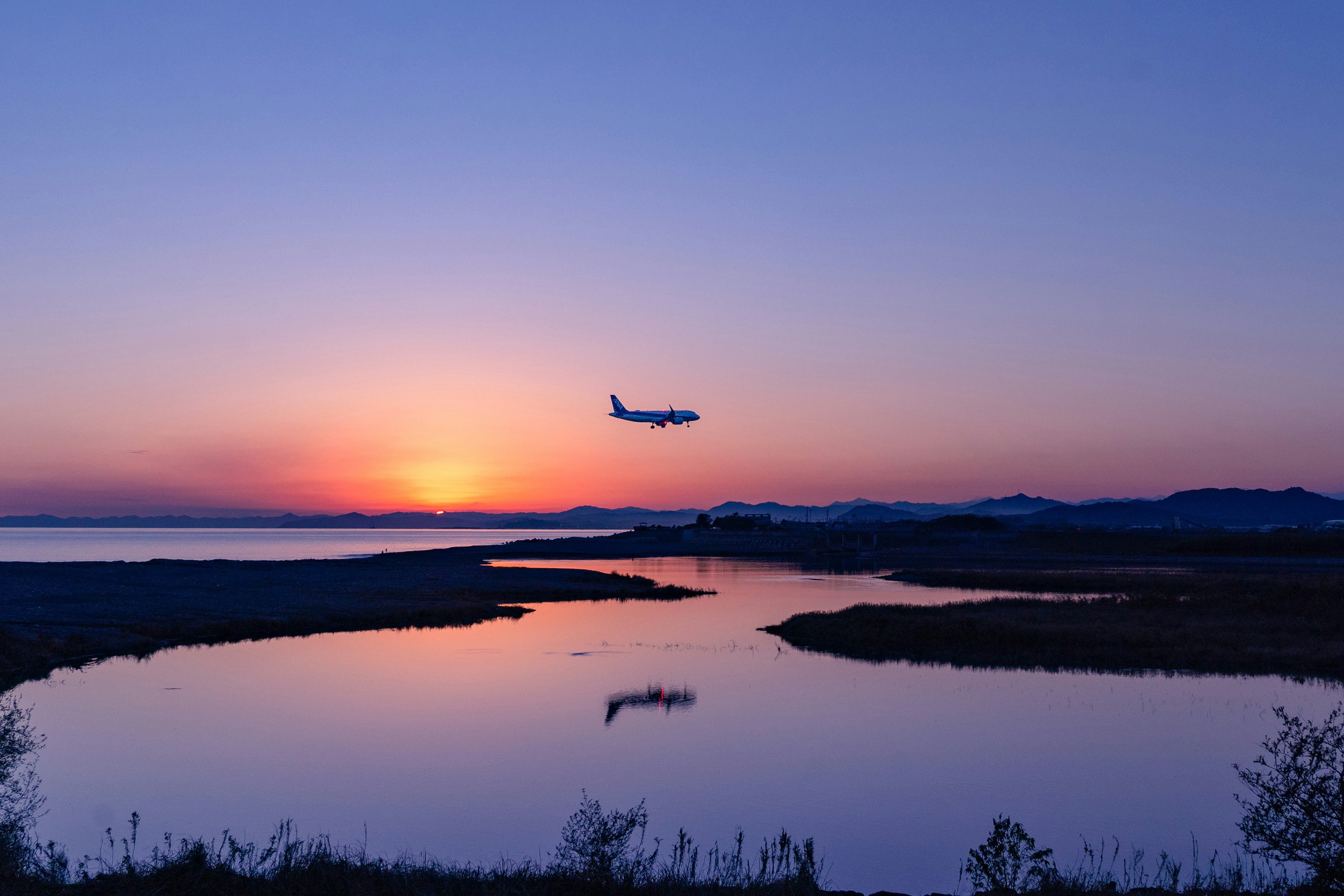 夕焼けの湖面に映る飛行機のシルエット