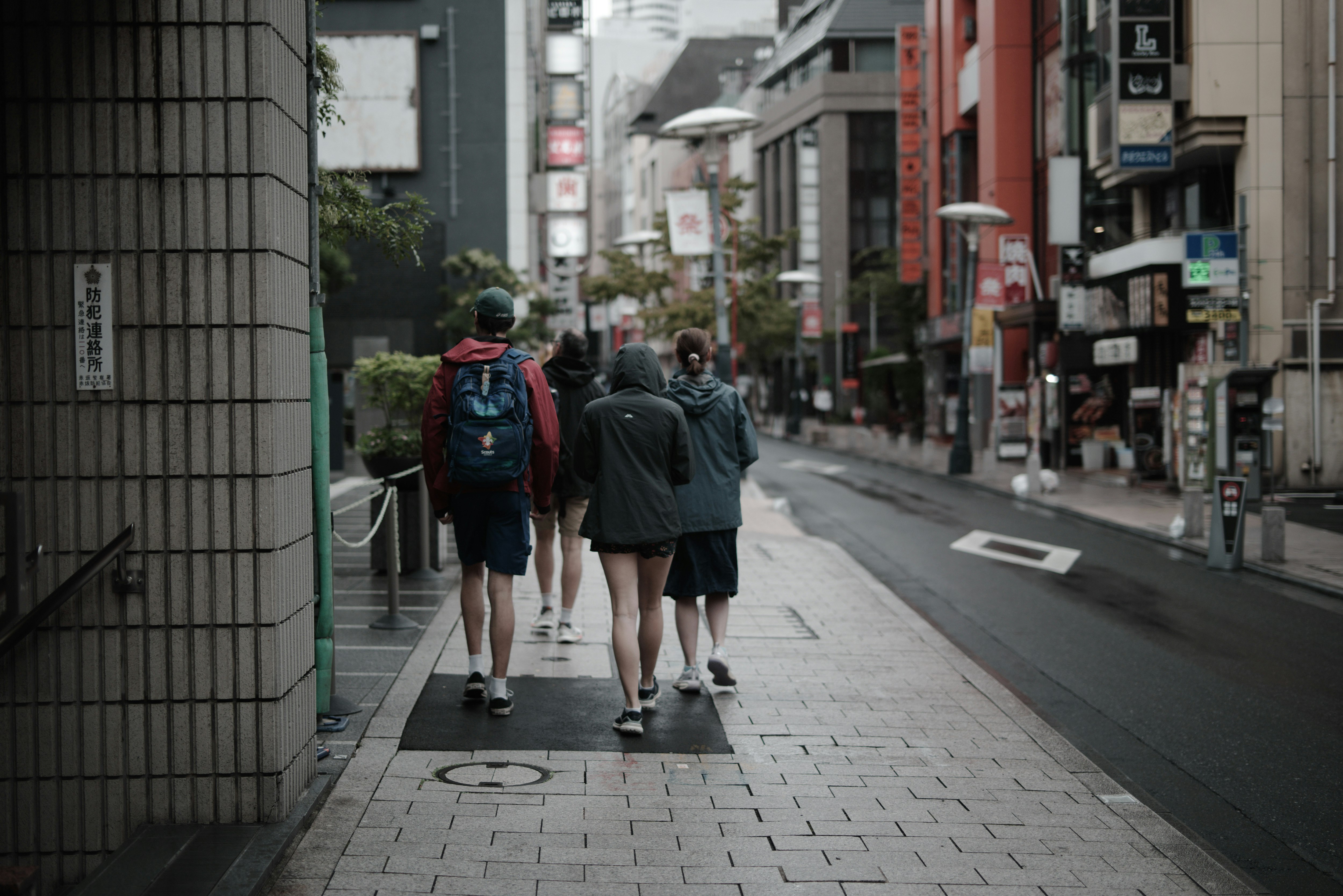 雨の降りはじめた一ツ木通りの路地を歩く人々の後ろ姿