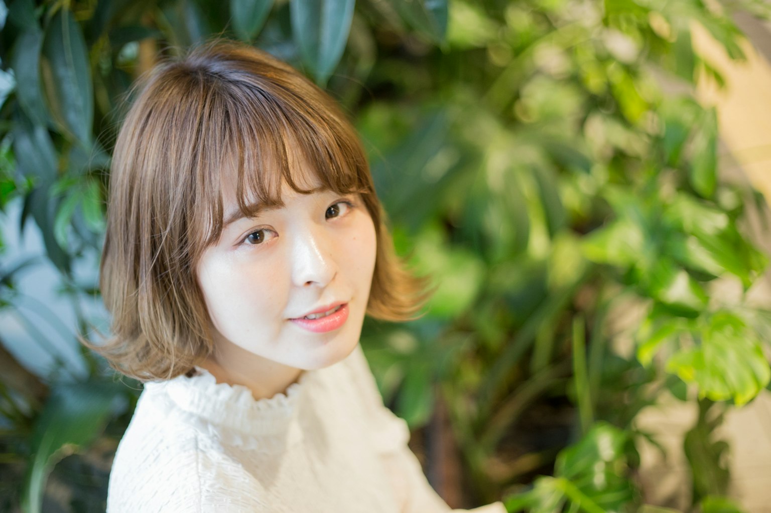 젊은 여성이 녹색 식물 배경에서 미소 짓고 있다
