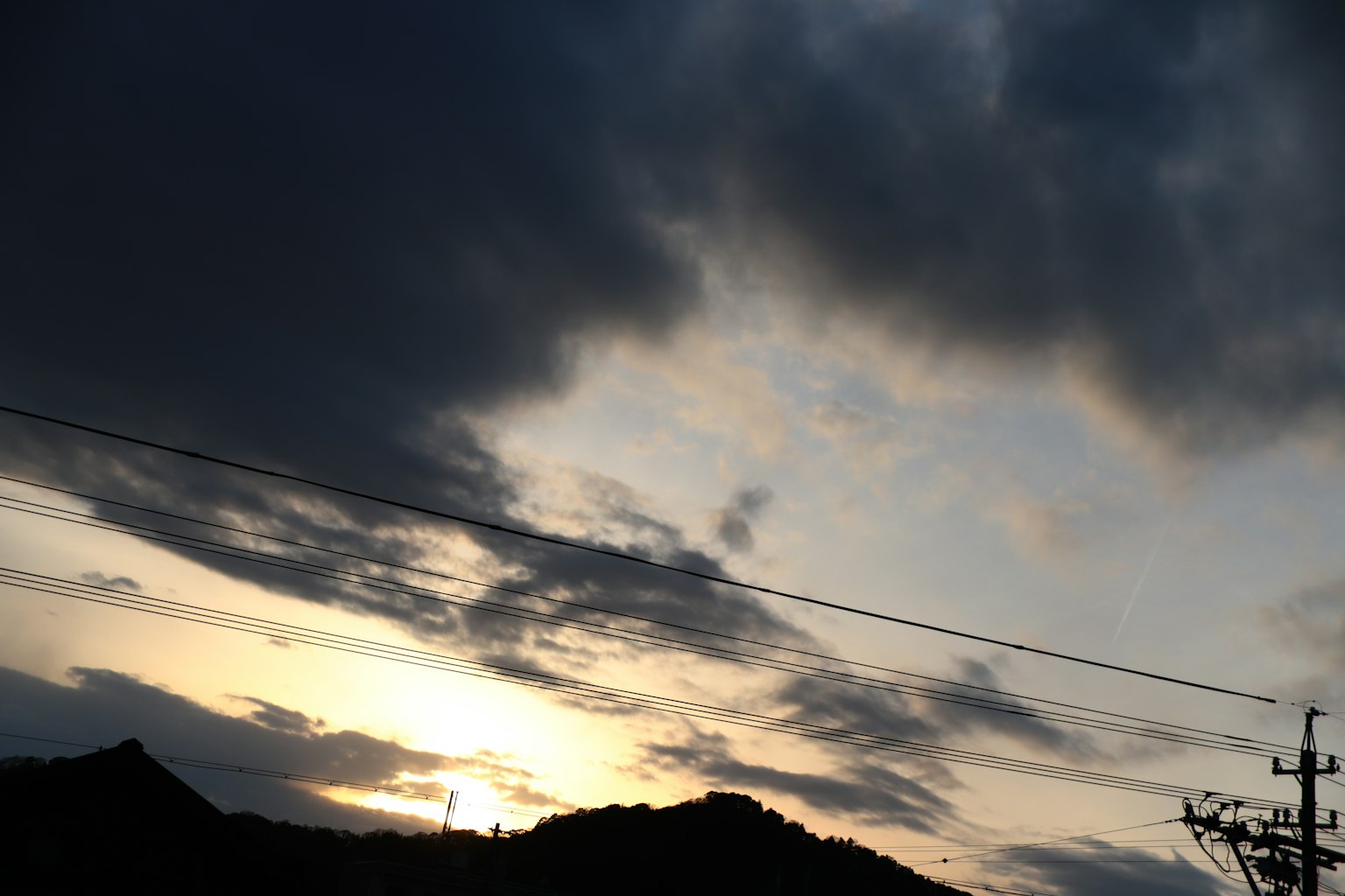 Dramatischer Sonnenuntergangshimmel mit silhouettierten Bergen und Stromleitungen