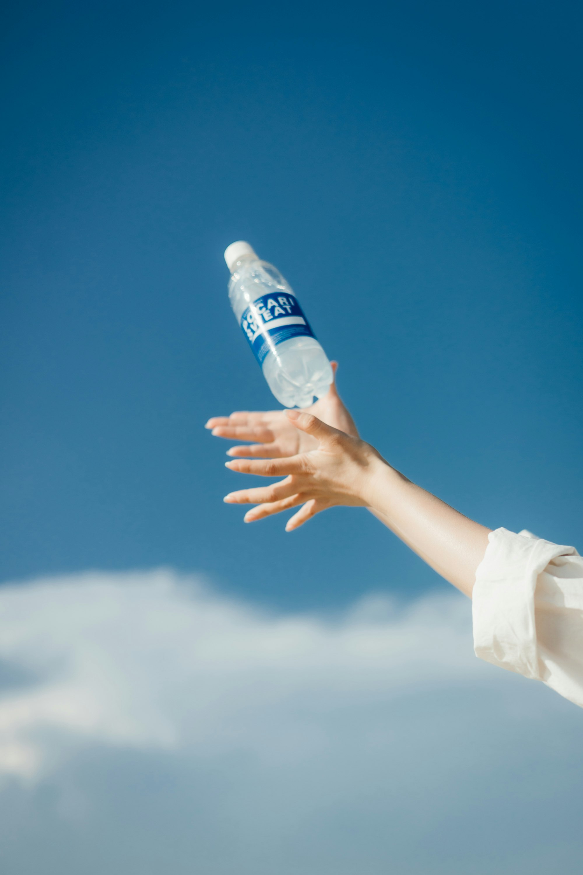 mains d’enfant offrant une bouteille en plastique contre un ciel bleu