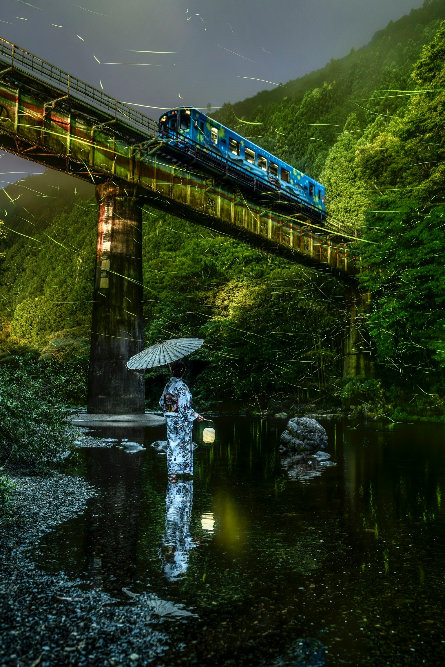 Un treno blu che attraversa un ponte in un paesaggio verdeggiante con una persona con un ombrello