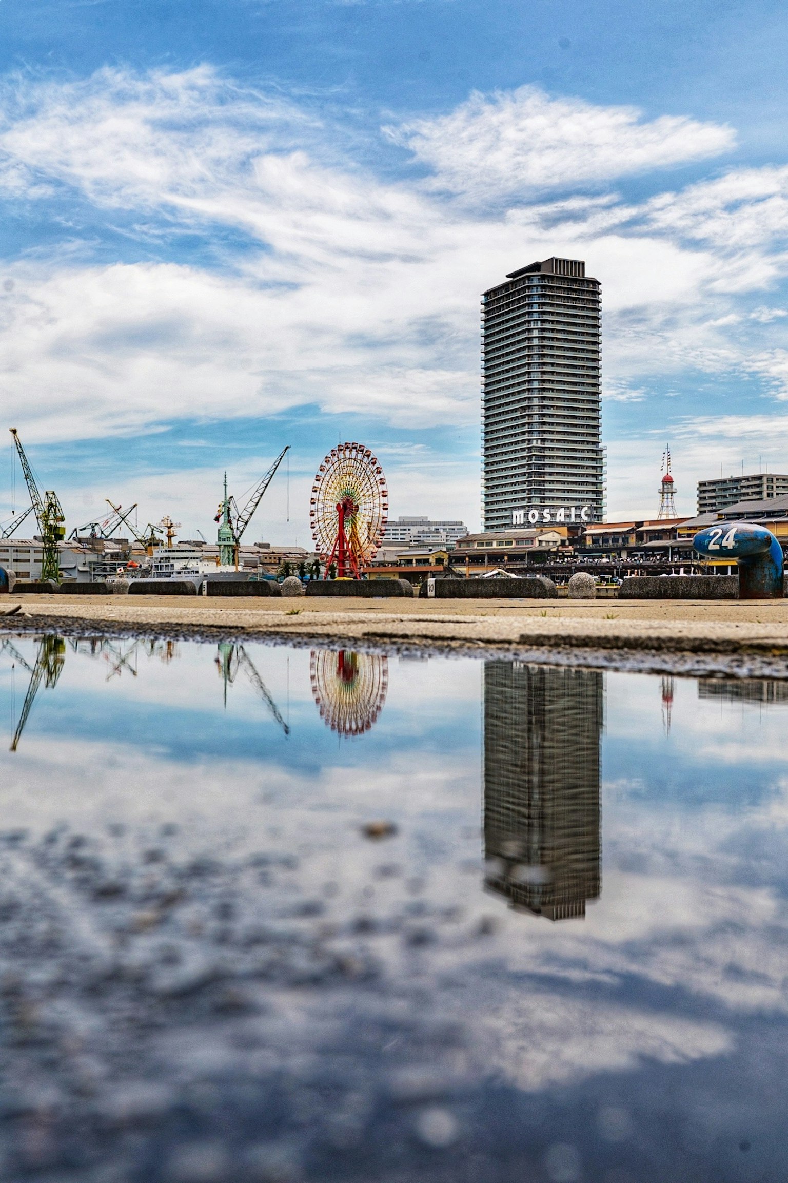 Horizonte de la ciudad con un edificio alto y una noria reflejados en el agua