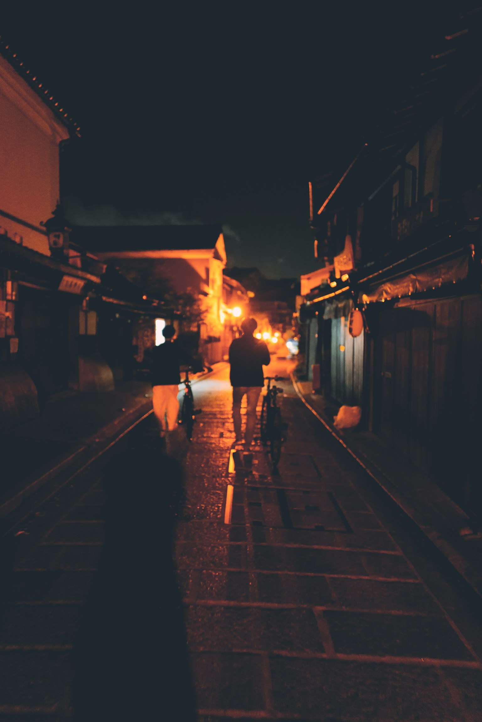 Silhouette di persone che camminano in una stretta via di notte con lampioni arancioni caldi