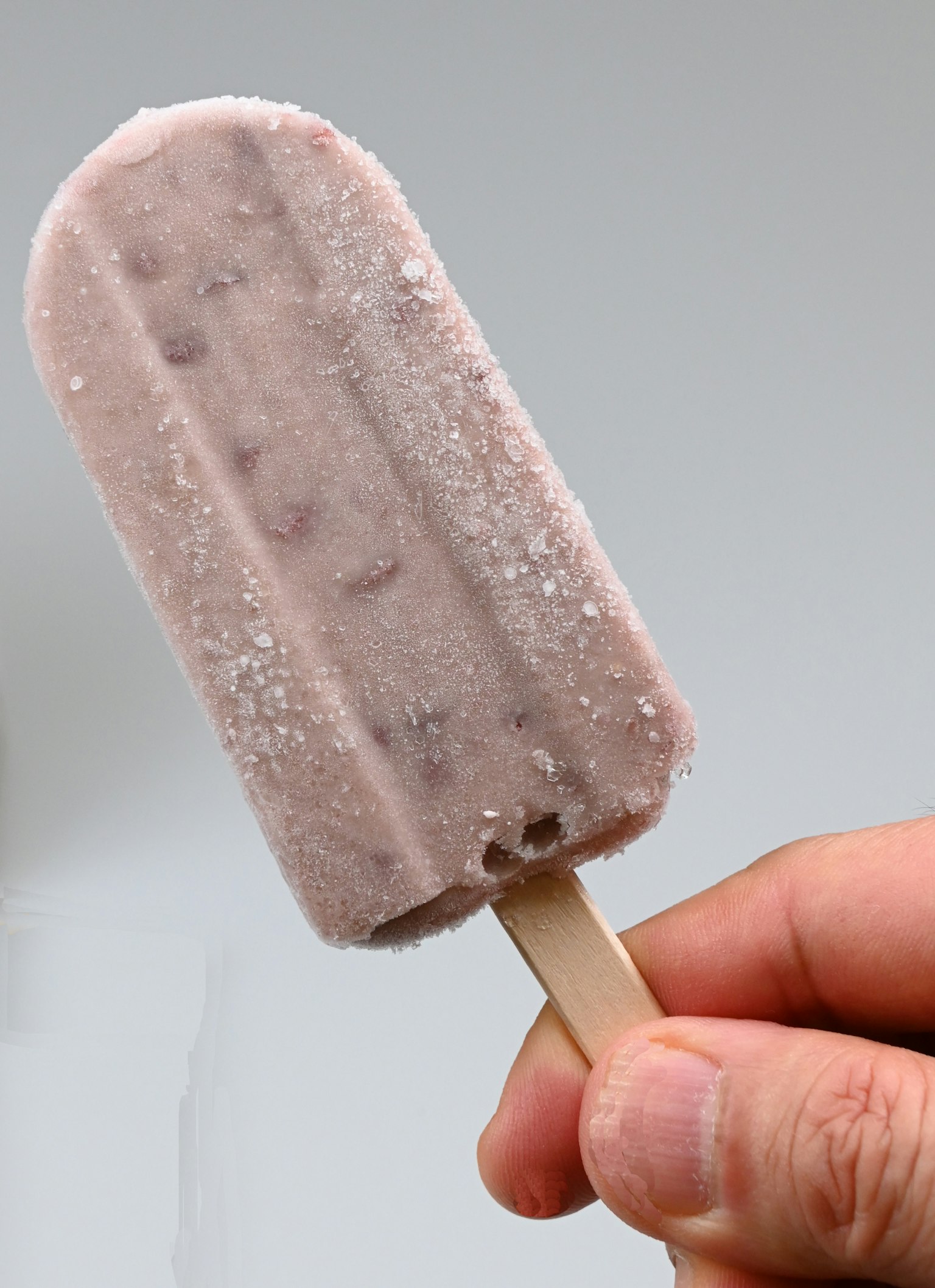 Una mano sosteniendo un helado de color púrpura pálido con cristales de hielo en la superficie