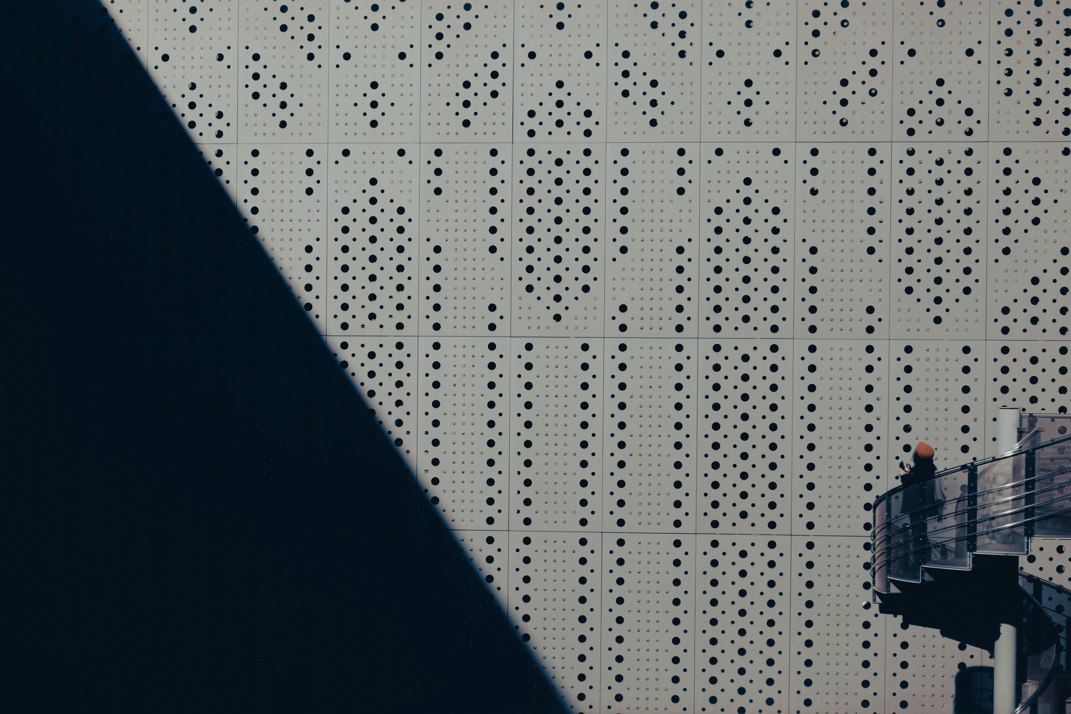 détail architectural d’un mur en métal perforé avec des ombres diagonales qui se croisent