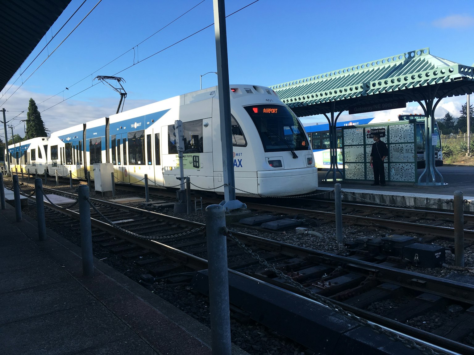 Un tren blanco con acentos azules deteniéndose en una estación bajo un cielo azul