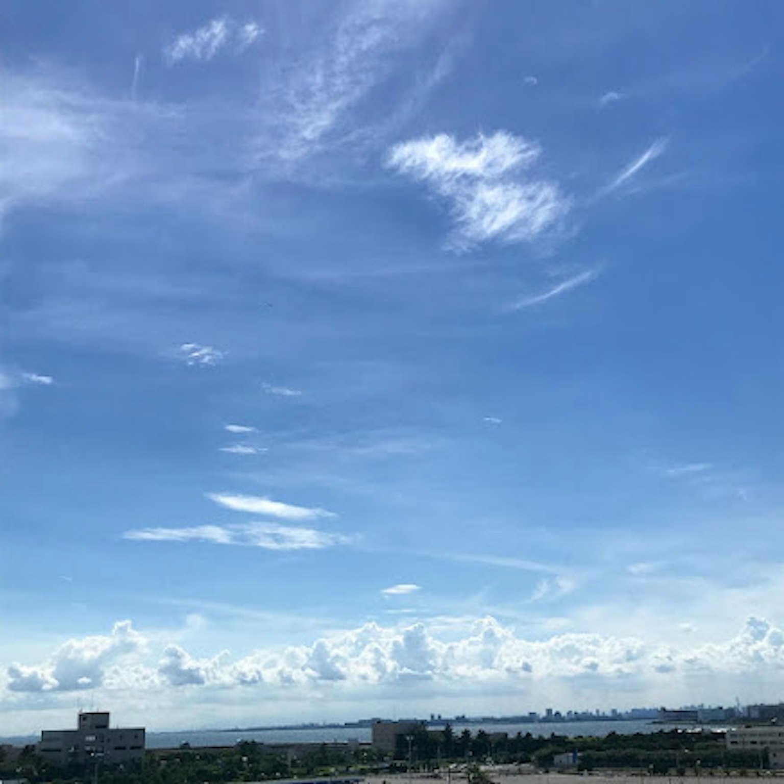 Cielo azul claro con nubes blancas sobre un horizonte urbano distante