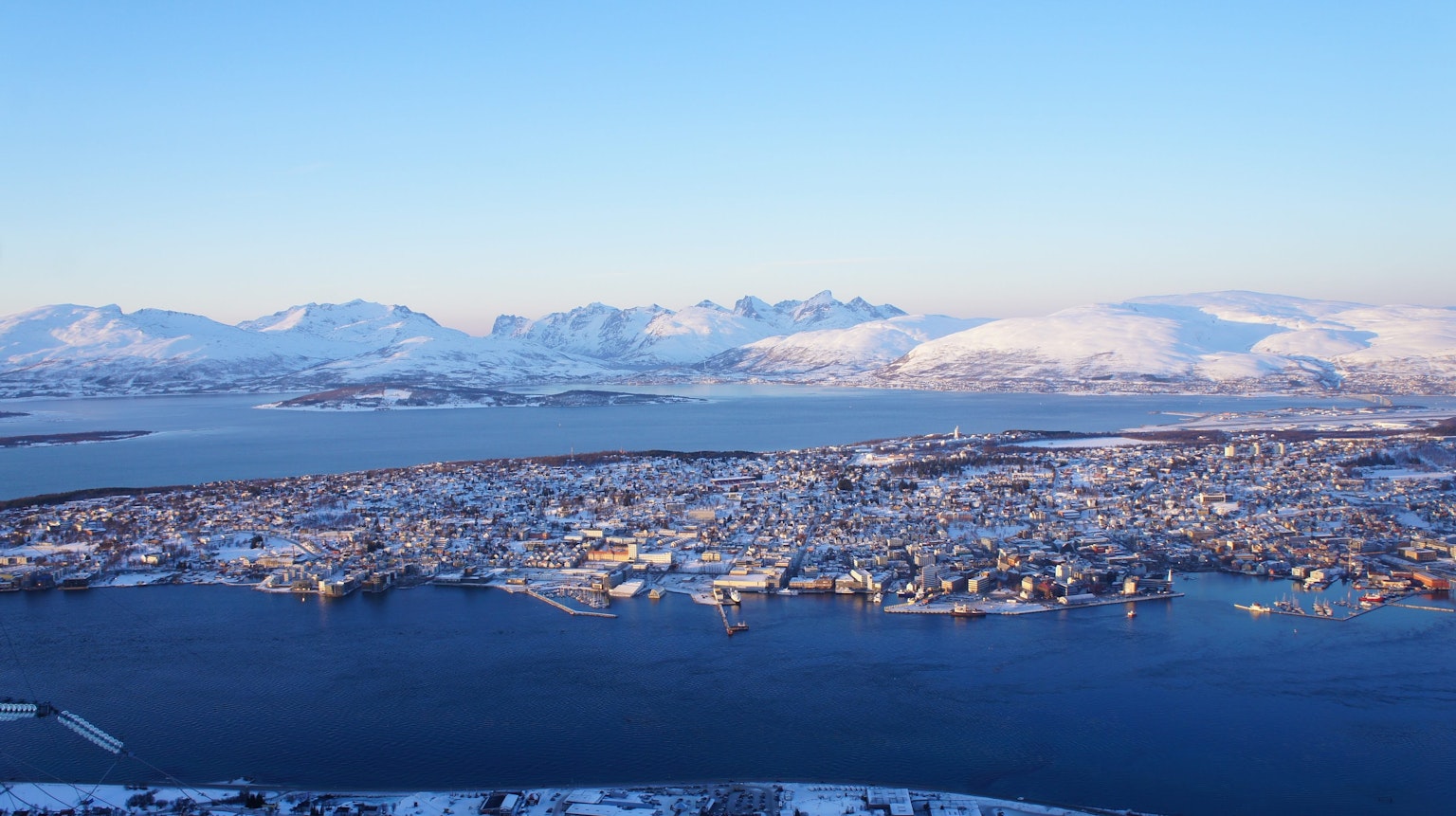Eine malerische Aussicht auf eine norwegische Stadt, umgeben von verschneiten Bergen und einer ruhigen Wasseroberfläche
