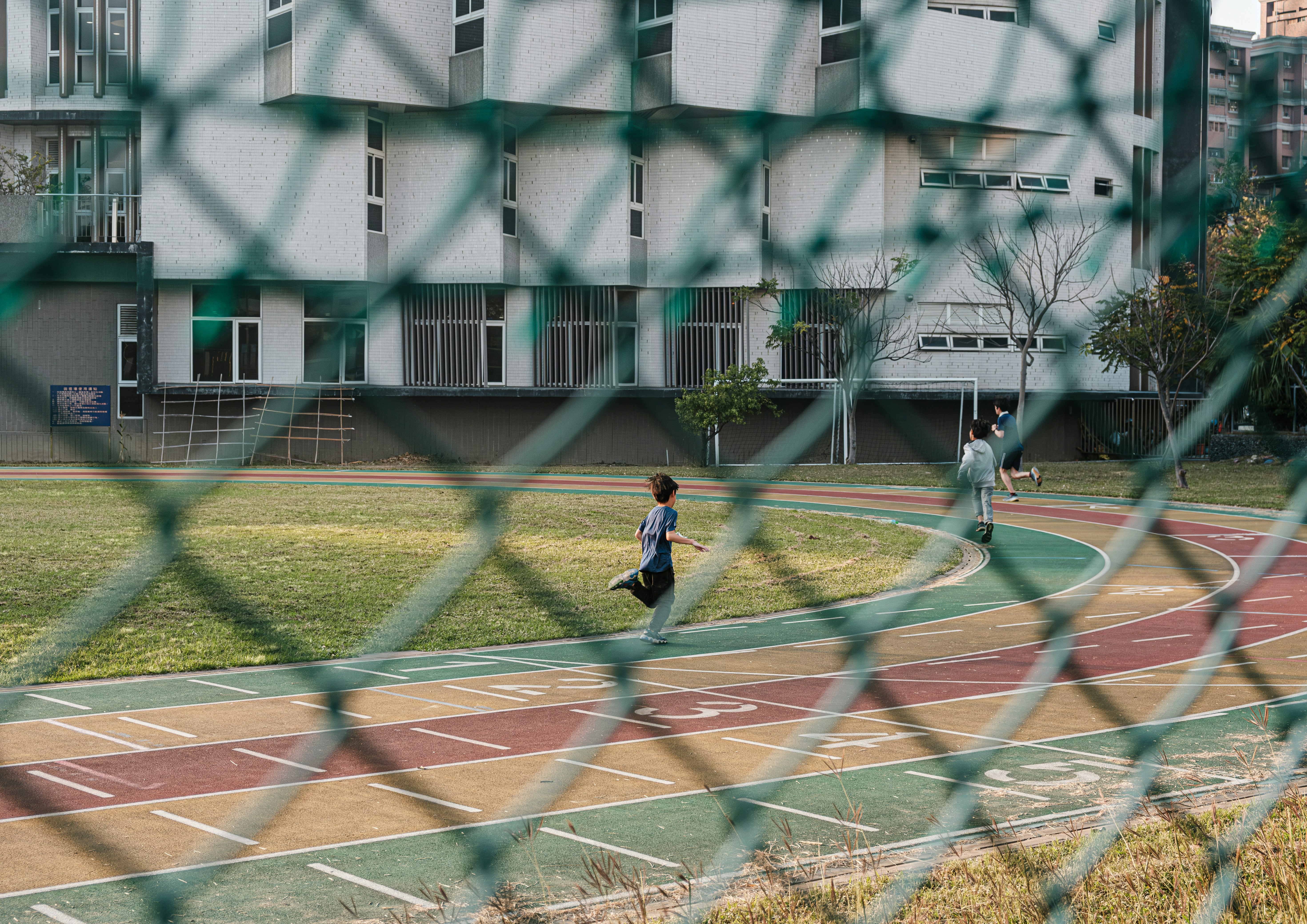 学校の運動場で走る人々とフェンス越しの風景