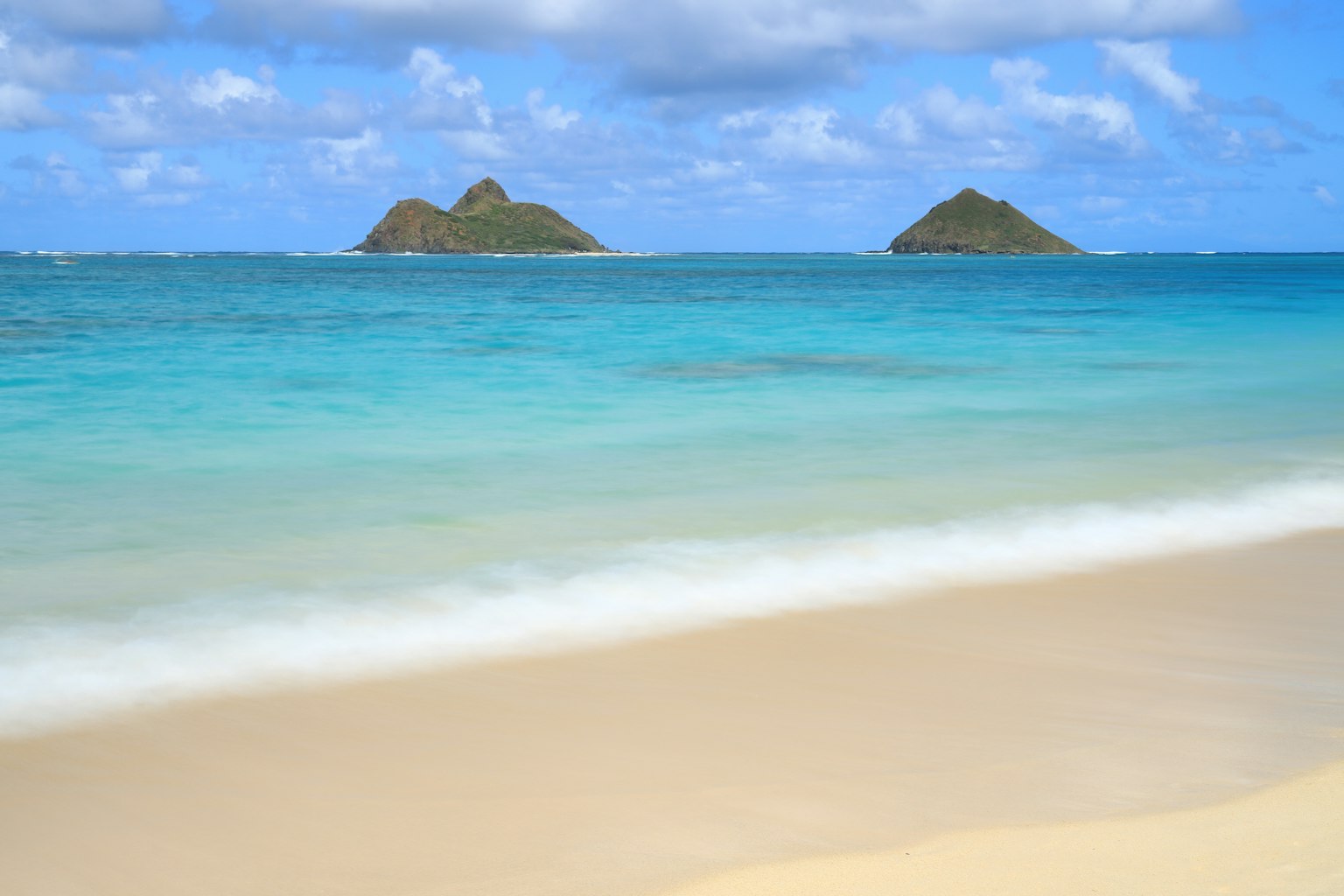 Scenic view of turquoise ocean and white sandy beach with two small islands