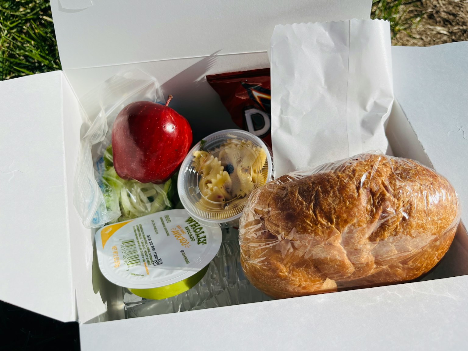Hộp ăn trưa chứa bánh sandwich, táo đỏ, salad, khoai tây chiên, nước sốt