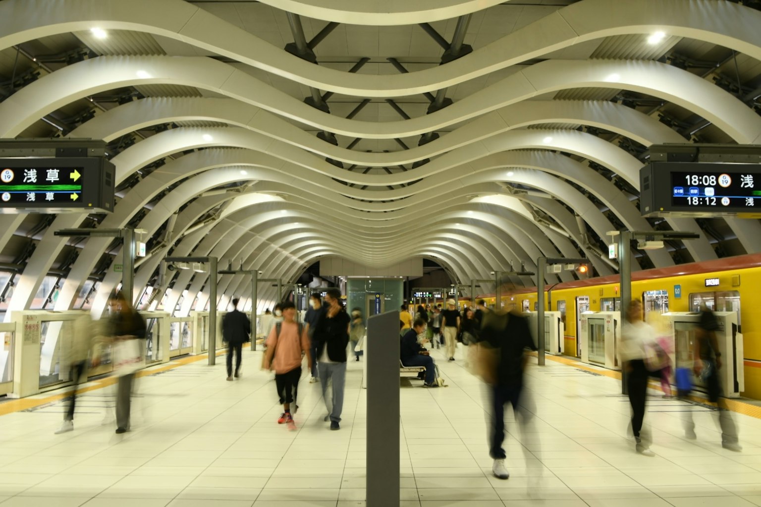 Interior moderno de estación de tren con personas caminando bajo un techo ondulado y luces brillantes