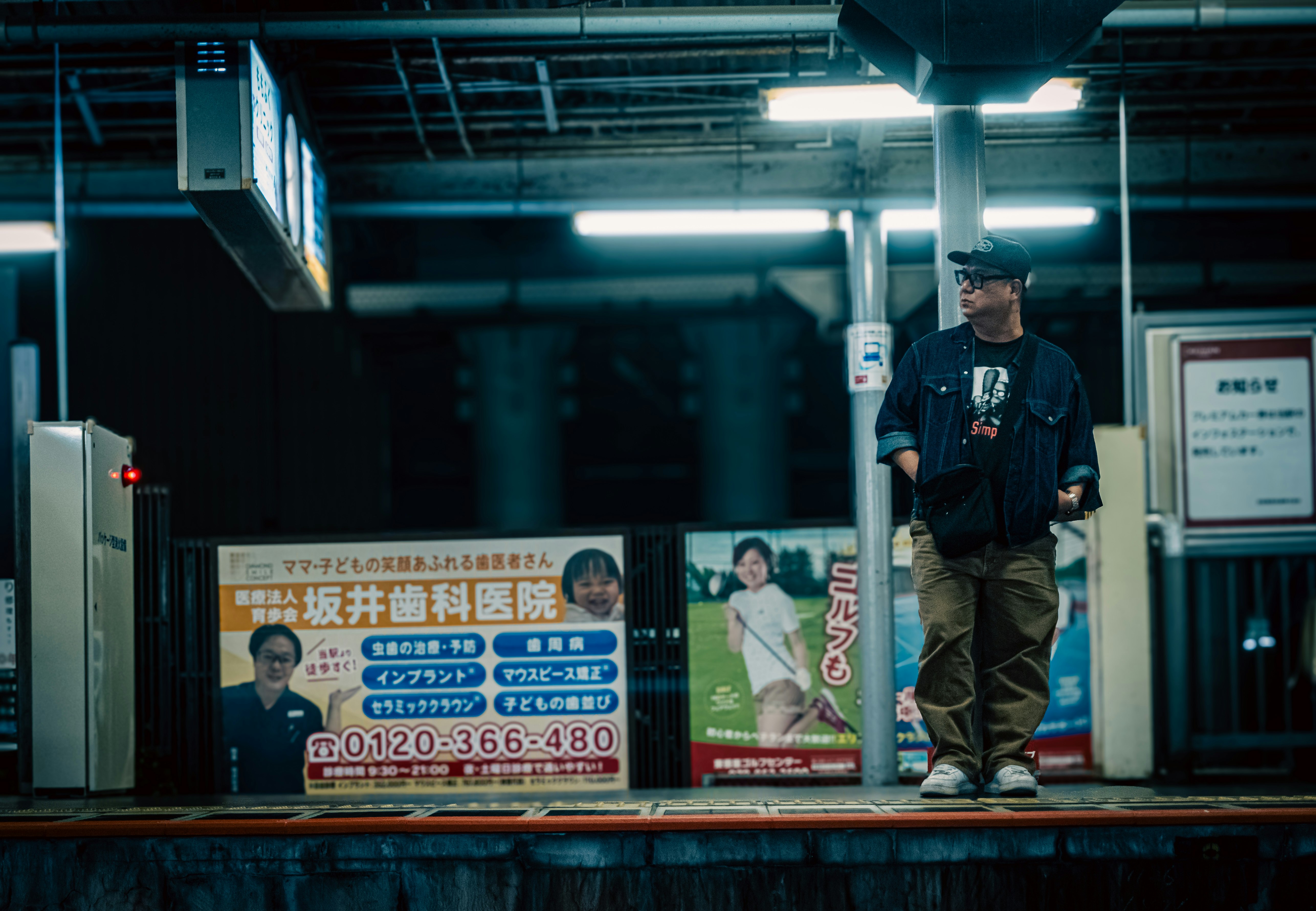 駅のホームで立つ作業員風の人物と掲示ポスターのある改札周辺