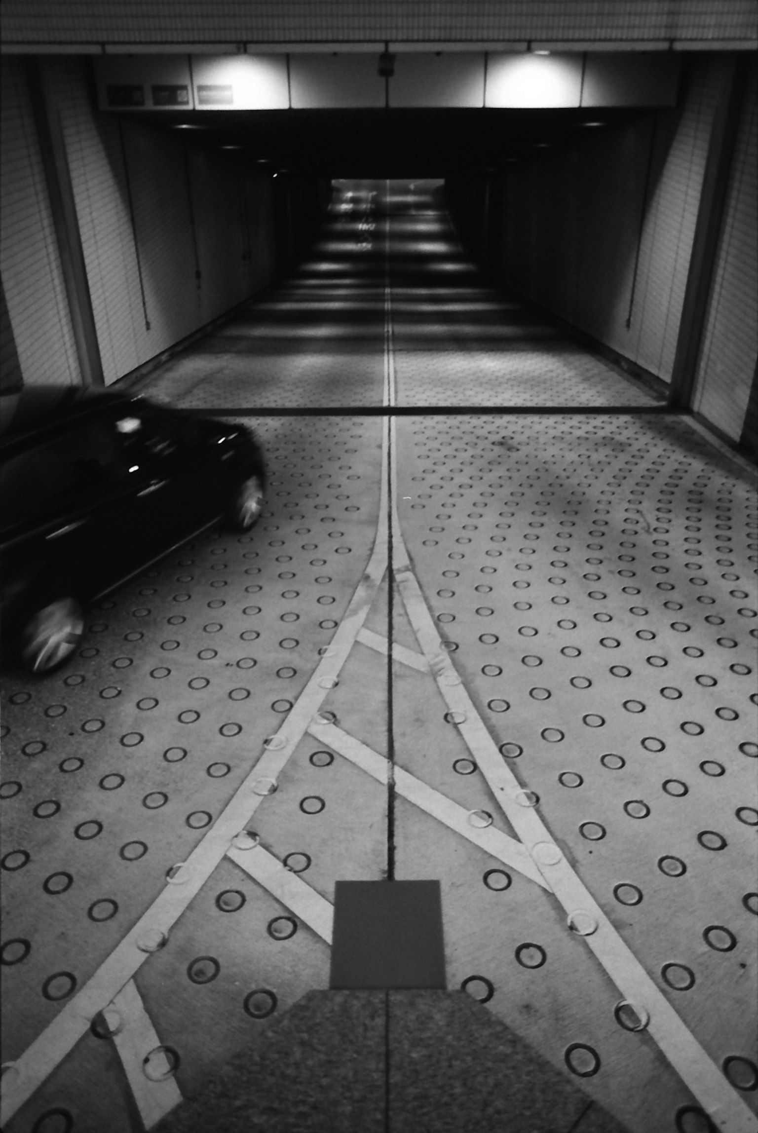 A black car driving on a patterned circular pavement inside a tunnel