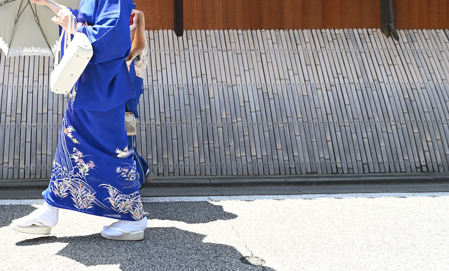 Una mujer con kimono azul caminando frente a una pared de madera