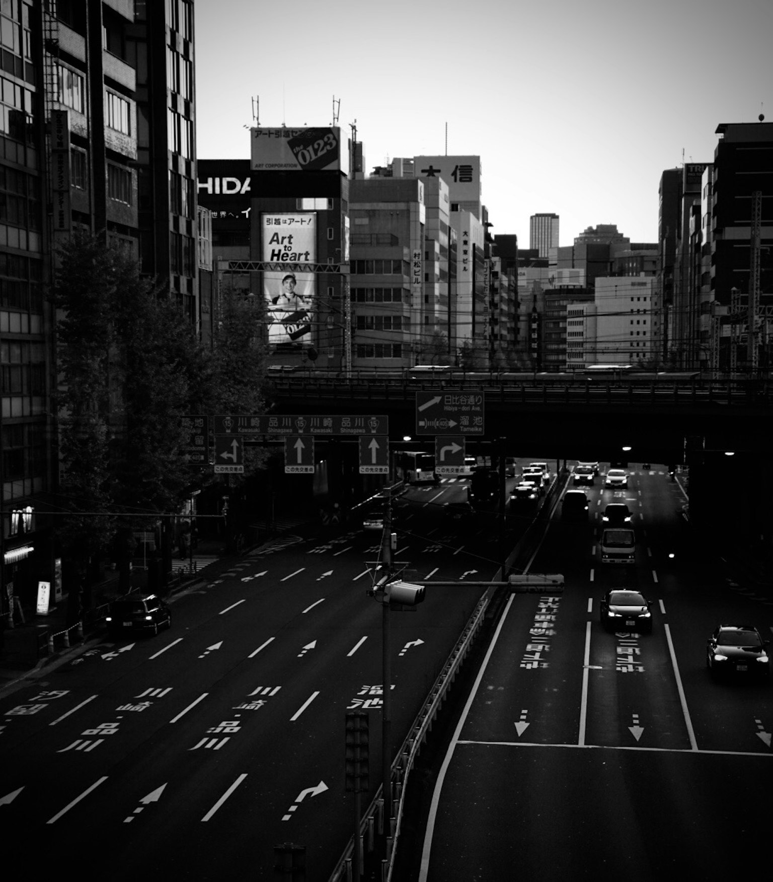 都市の高架道路とビル群のモノクロ画像 交通の流れと看板が見える
