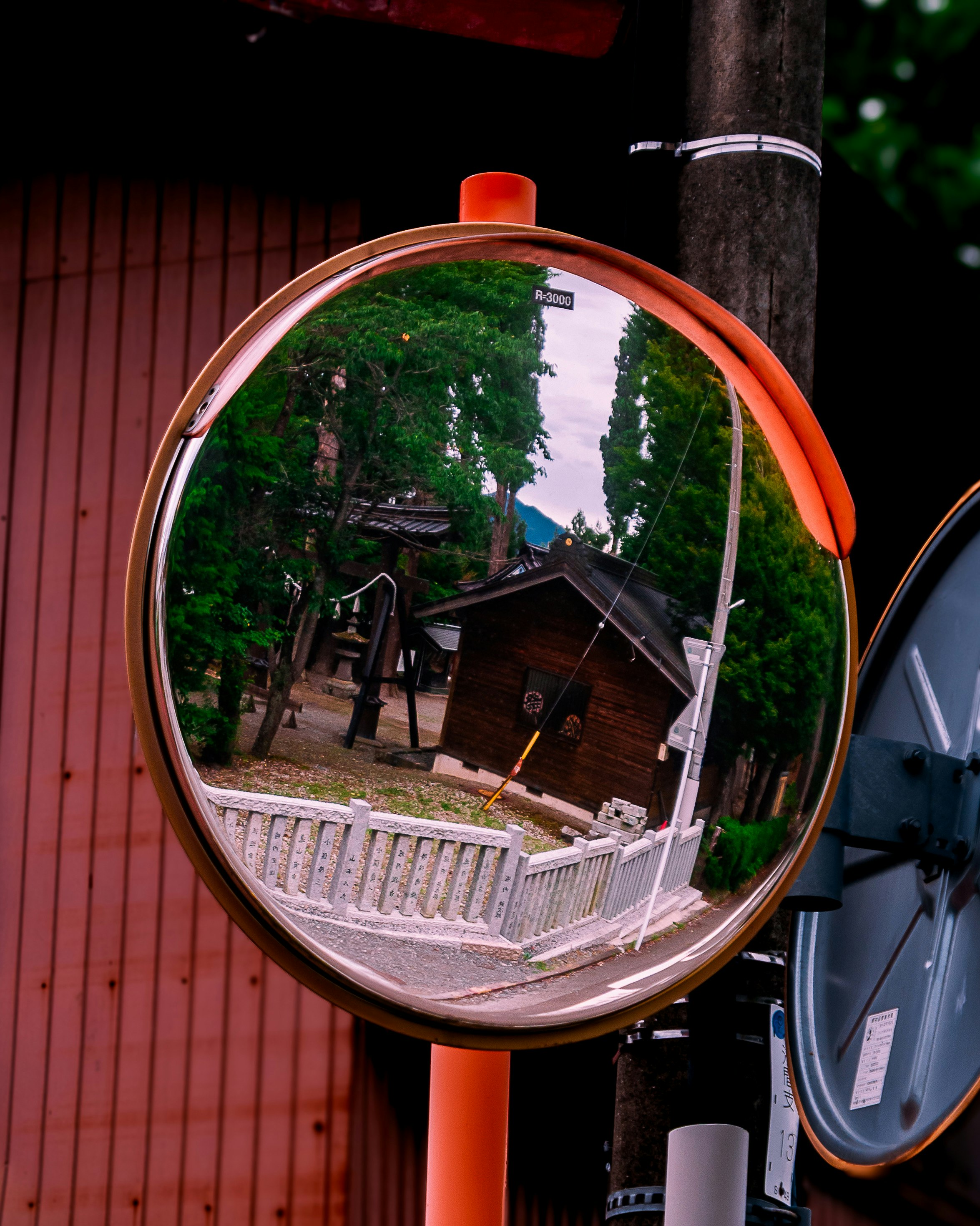 Miroir rond sur un poteau rouge reflétant une maison en bois et un jardin