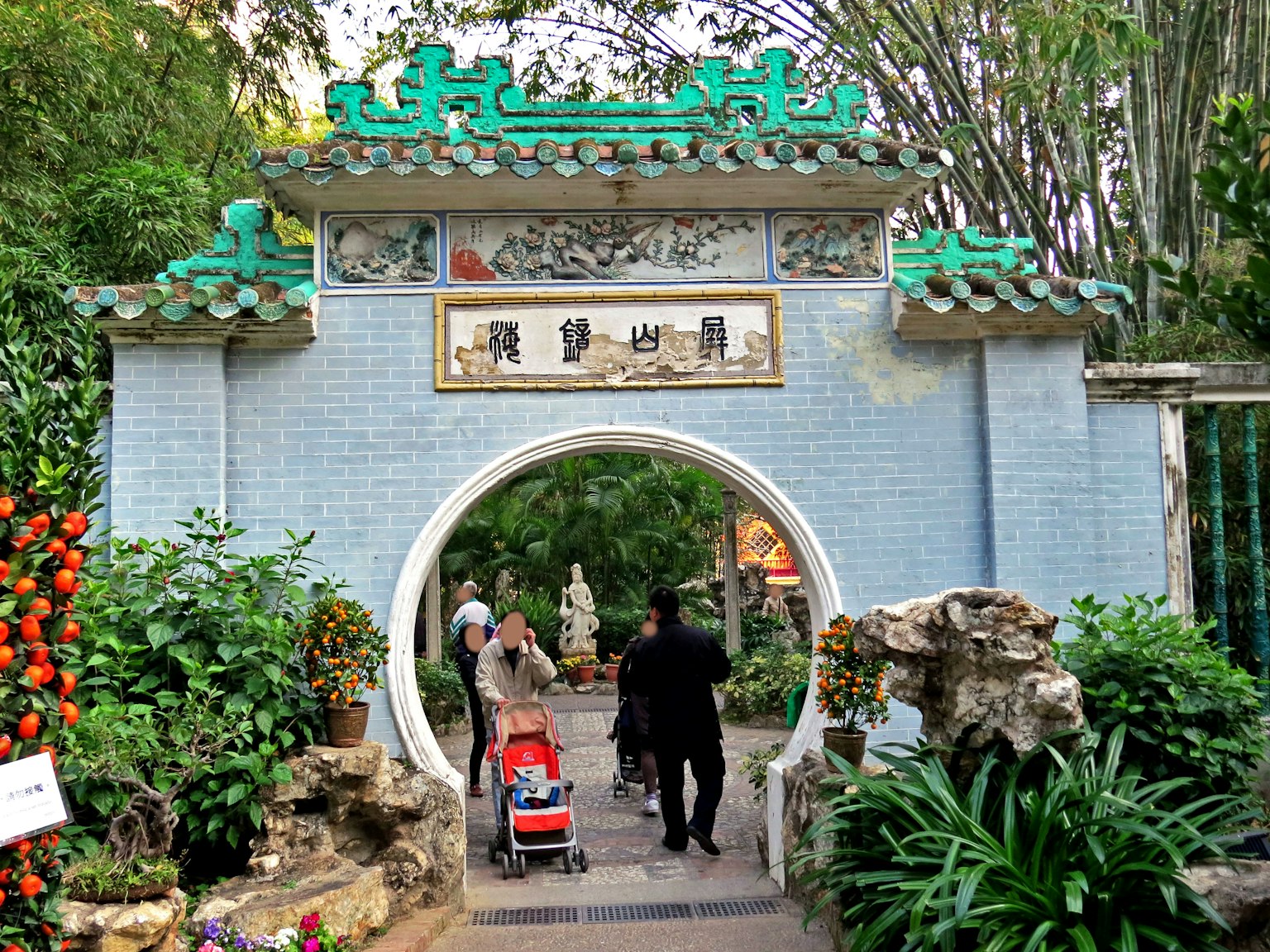 Entrata di un giardino in stile cinese con un arco a tetto verde e visitatori che attraversano